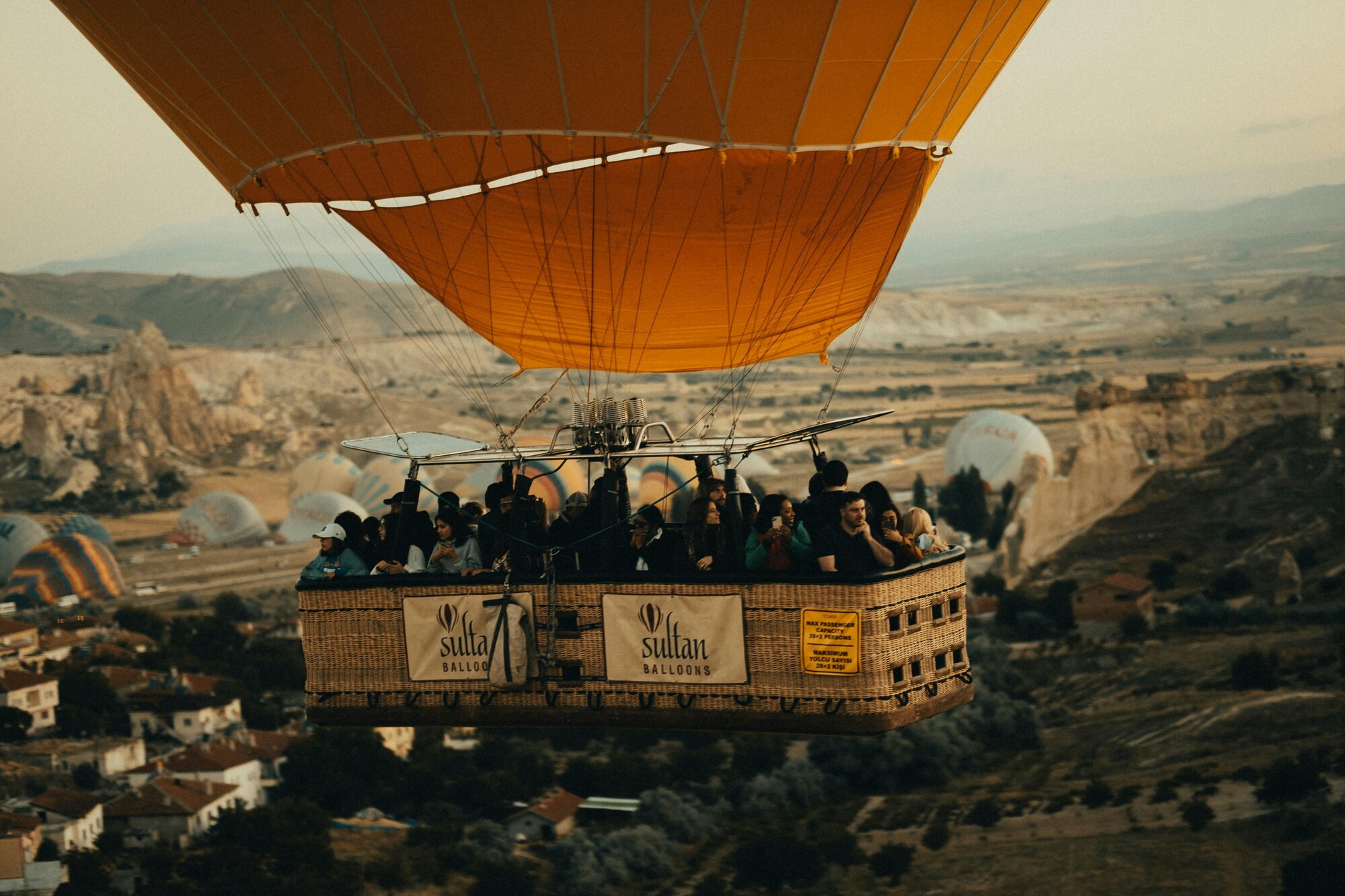 A hot air balloon with a basket carrying passengers flying over a landscape with other hot air balloons in the distance.