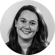 Schwarz-weiß-Porträt einer jungen Frau mit lockigem Haar, lächelnd gegen einen grauen Hintergrund.