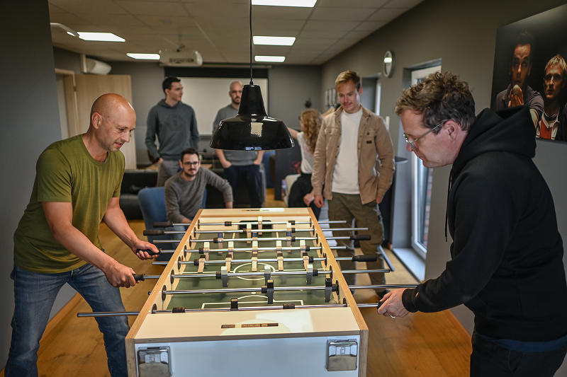 Sieben Männer spielen Tischfußball in einem modernen Raum, während andere zuschauen.