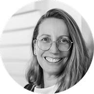 Schwarz-Weiß-Bild einer Frau mit Brille, lächelnd, vor einem Hintergrund mit horizontalen Linien.