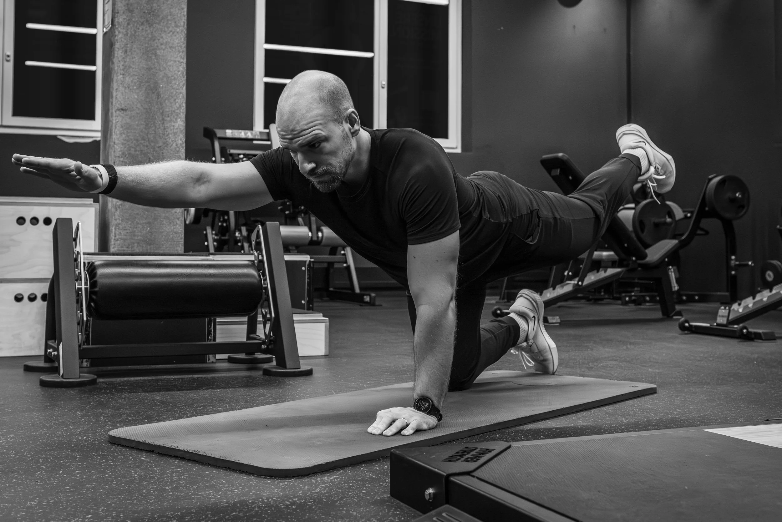 Mann macht eine Yoga- oder Balanceübung auf einer Yogamatte im Fitnessstudio, er befindet sich in einer seitlichen Planke mit ausgestrecktem Arm.