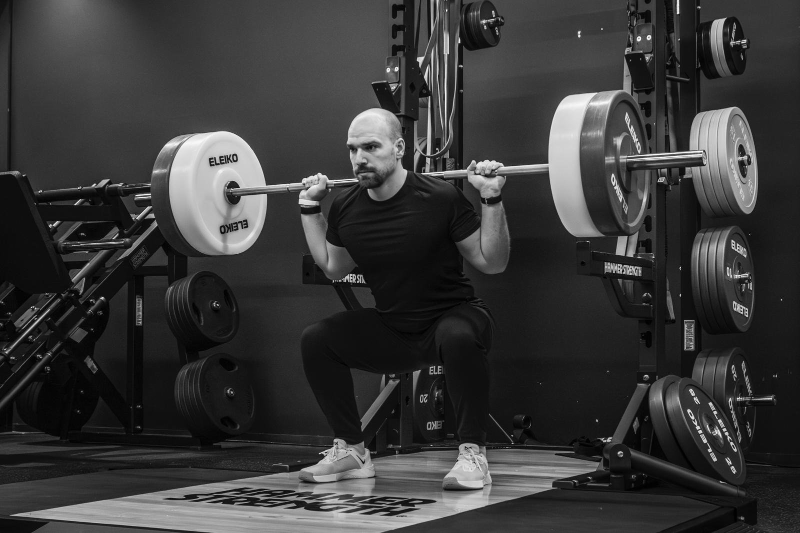 Mann beim Kniebeugen mit Langhantel in einem Fitnessstudio.