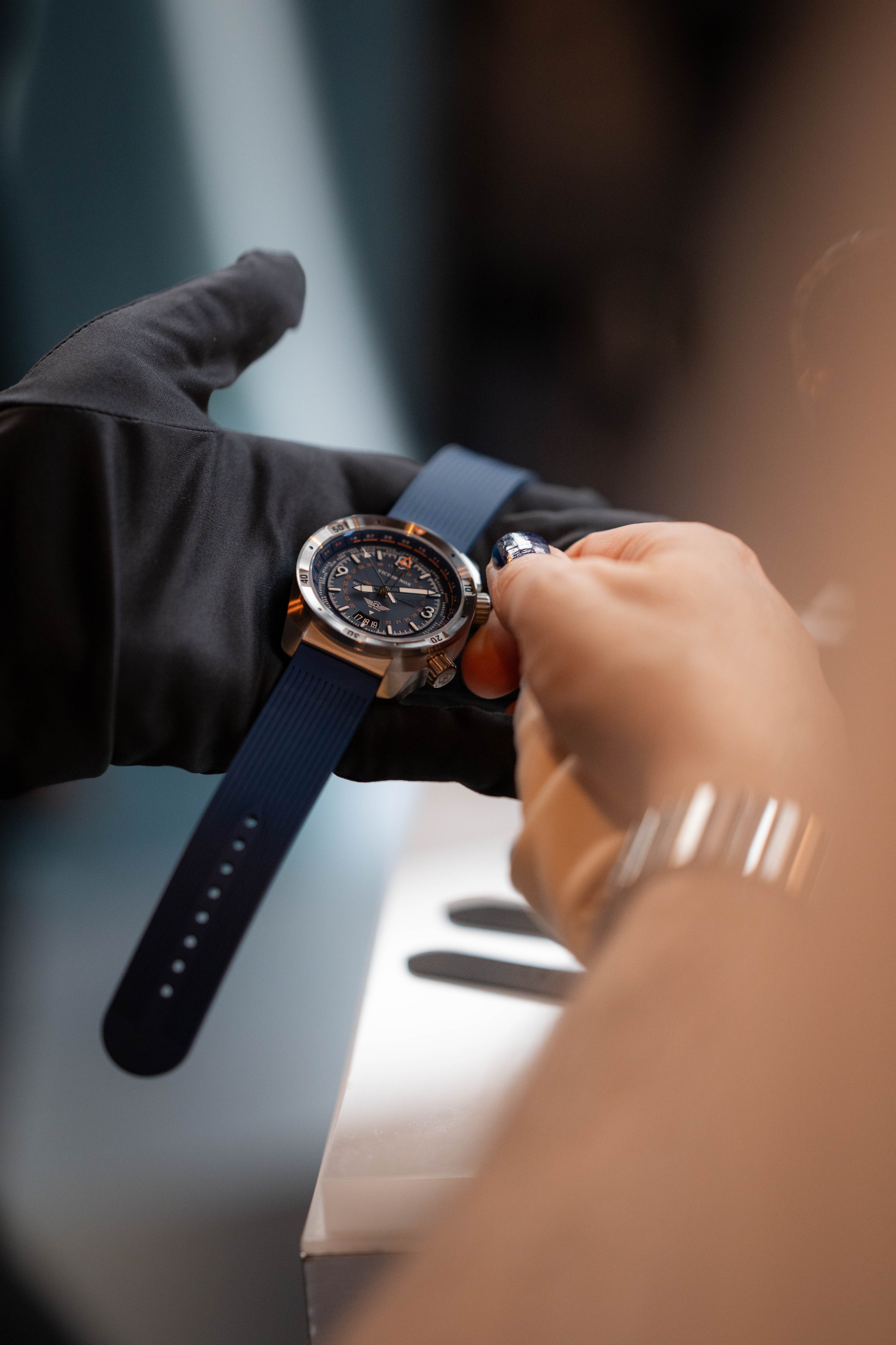 Person prüft eine Armbanduhr mit blauer Silikonband, während sie eine schwarze Handschuh trägt.