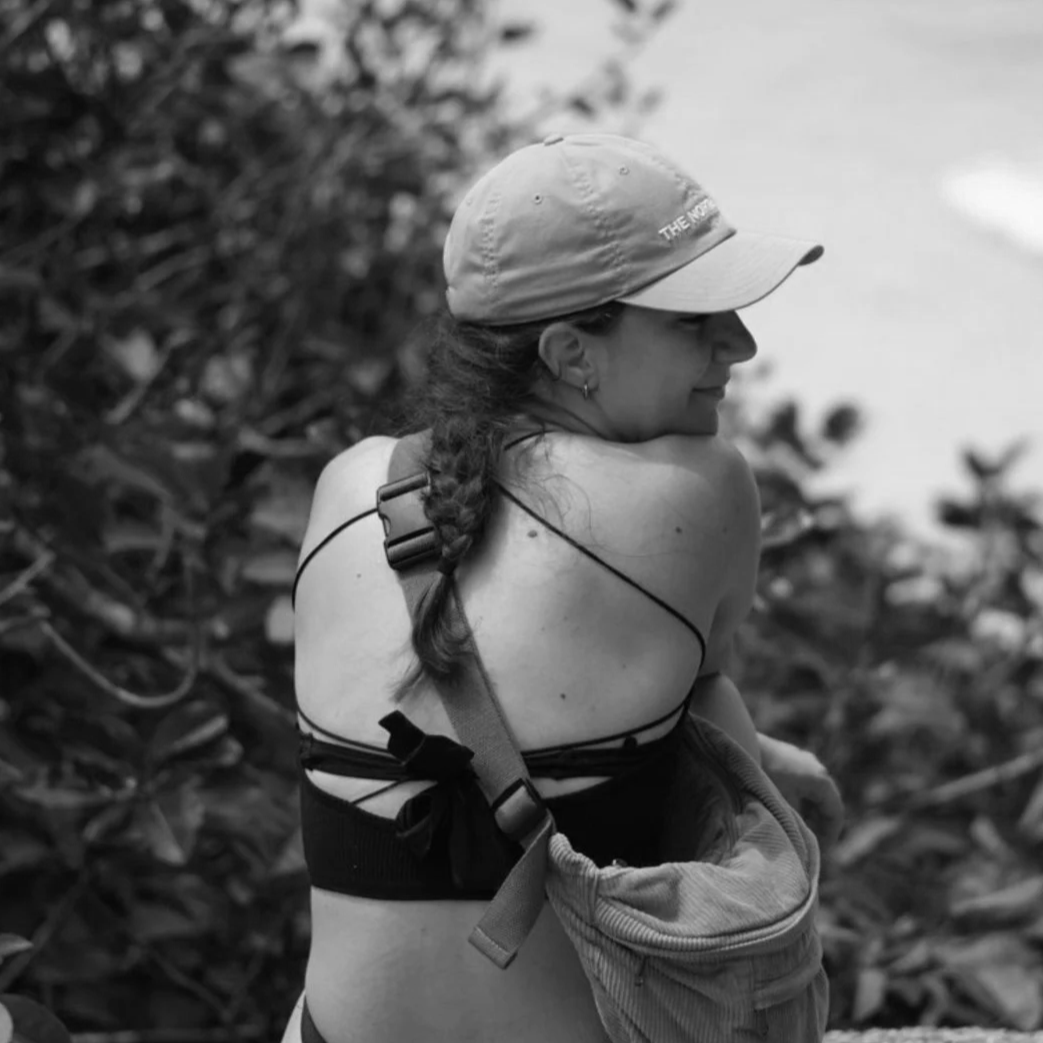 Frau mit Baseballcap und Rucksack, in einer natürlichen Umgebung, vermutlich am Wasser, lächelnd und nachdenklich. Ernährungswissenschaften und Ernährungsberatung und Fitness.