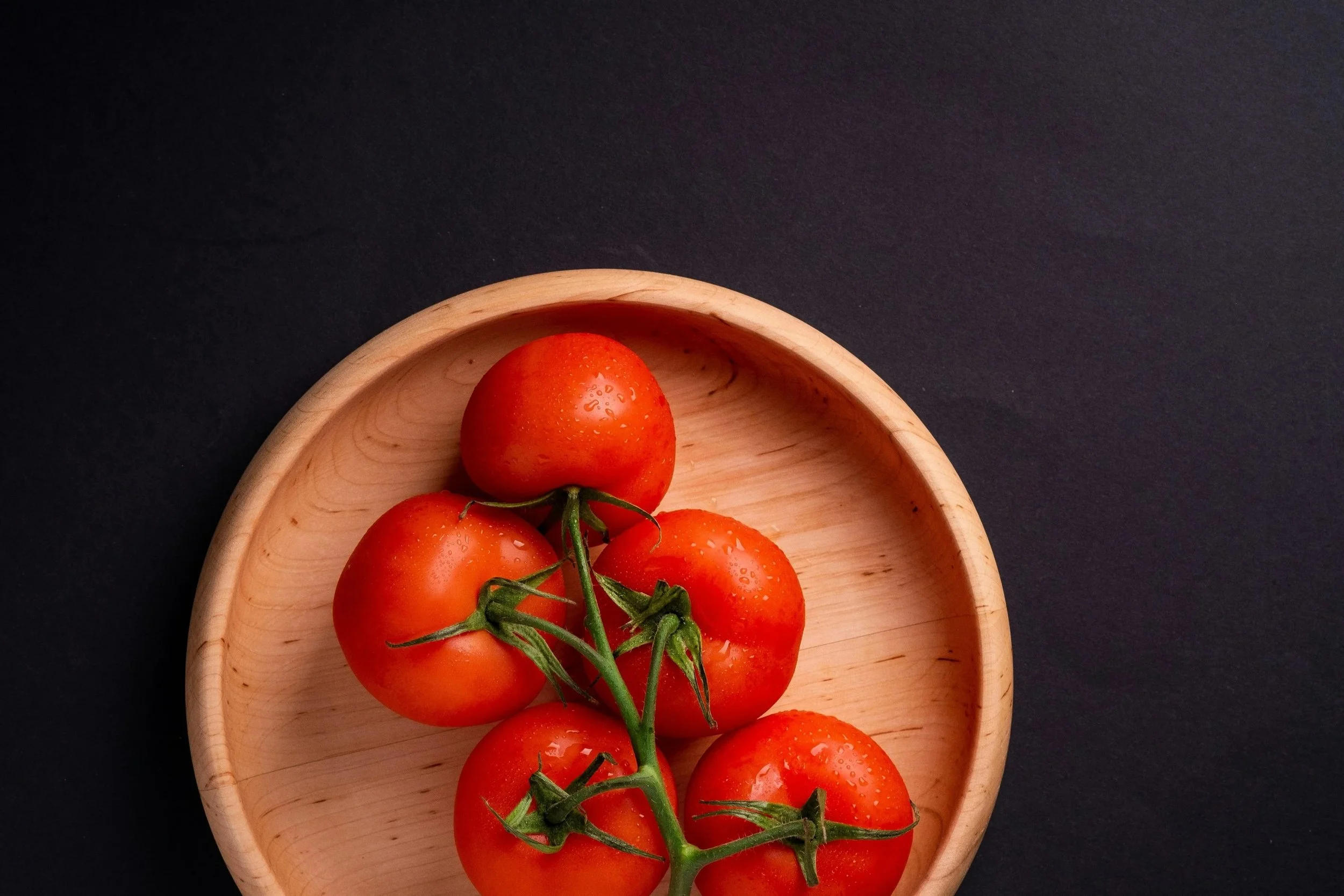 Rote Tomaten mit Wassertröpfchen auf einem Holztablett auf schwarzem Hintergrund. Ernährungswissenschaften und Ernährungsberatung und Fitness.