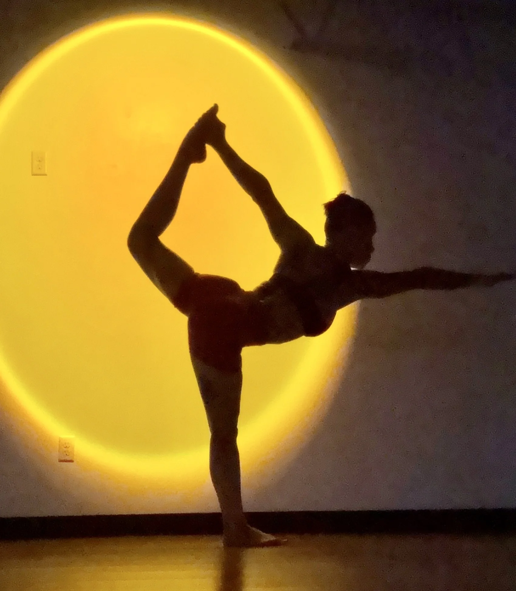 Silhouette of a ballet dancer performing a standing split pose with a yellow circular background.