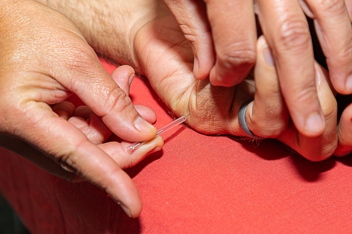 Person administering a shot with a needle to another person’s arm.