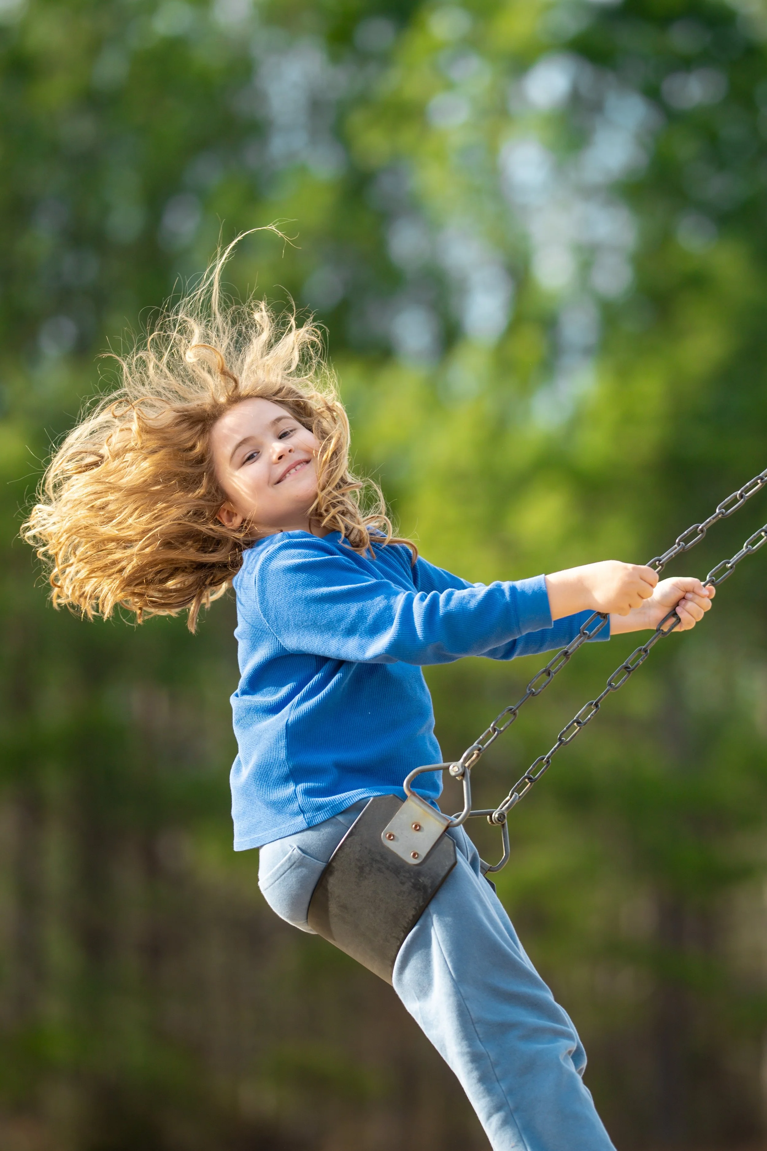 Meisje op een schommel in een bos met groene bladeren, lachend en spelend.