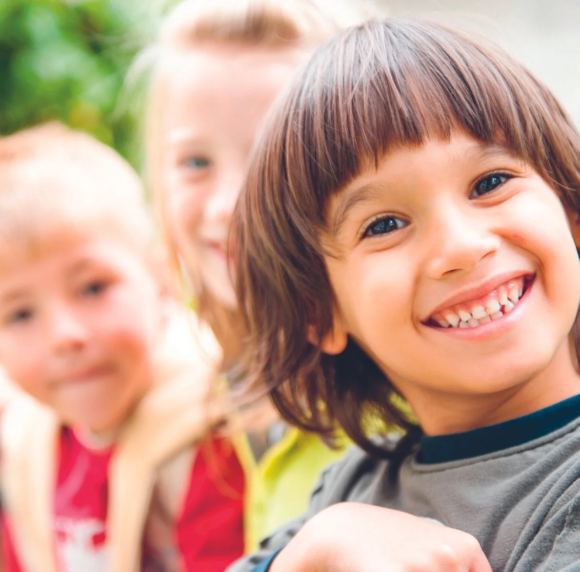 Drie lachende kinderen buiten, met een groene achtergrond.