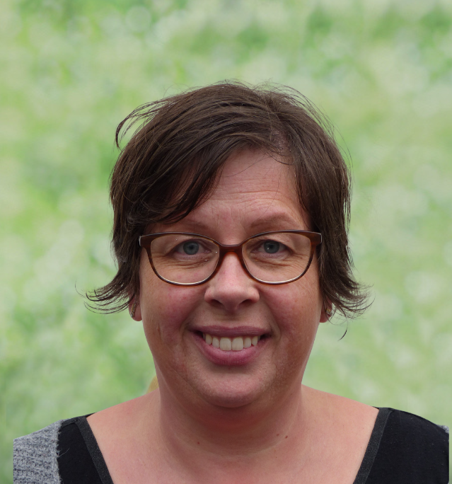 Portret van een vrouw met rood haar en grote oorbellen, lachend, op een lichte achtergrond.