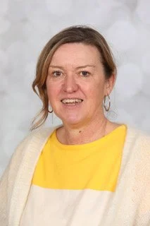 Portret van een vrouw met korte bruin haar die lacht, gekleed in een zwarte blazer, tegen een lichtgrijze achtergrond.