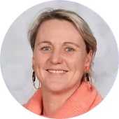 Een close-up van een lachende vrouw met kort blond haar, earrings en een roze vest.