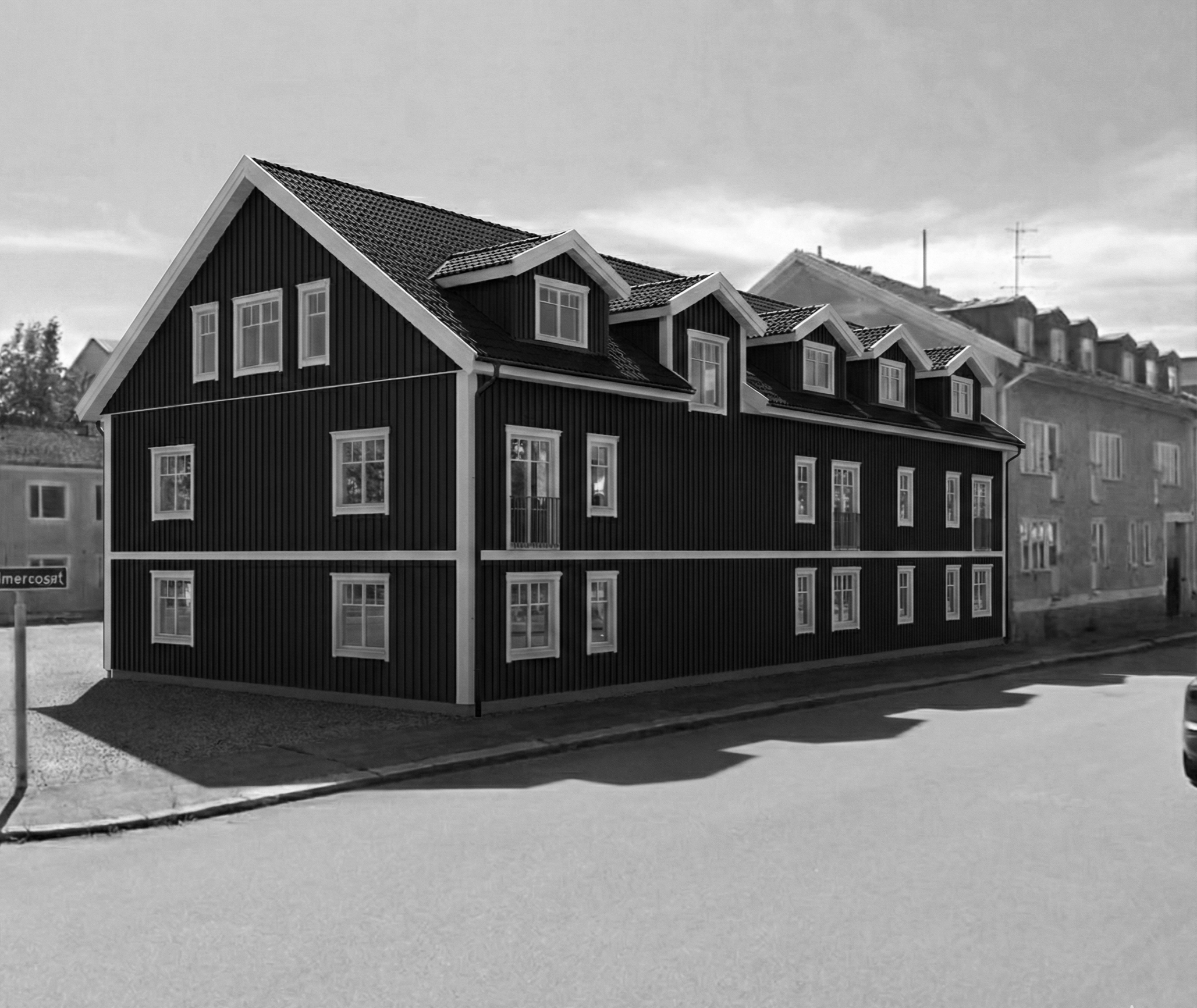 Black wooden building with multiple windows and dormer windows on the roof, situated on a street with shadows on the road and neighboring buildings in the background.