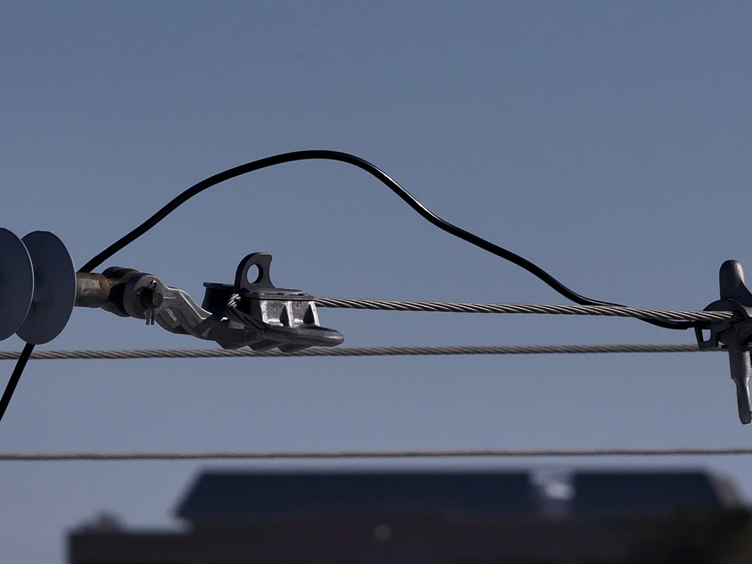 Close-up of a utility cable on a power line, with insulators and metal fixtures against a clear blue sky.