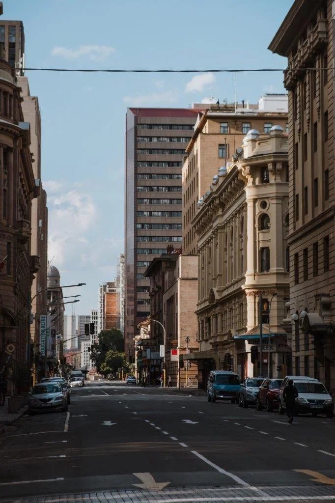 Empty city street with parked cars, historic and modern buildings, and a blue sky with a few clouds.