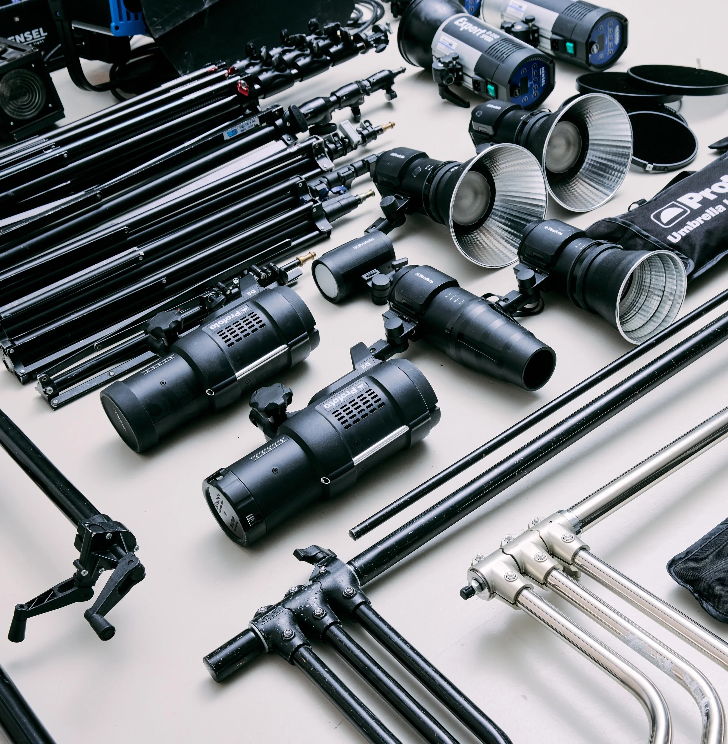 Photographic equipment including tripods, studio lights, and reflective dish lights arranged on a table.