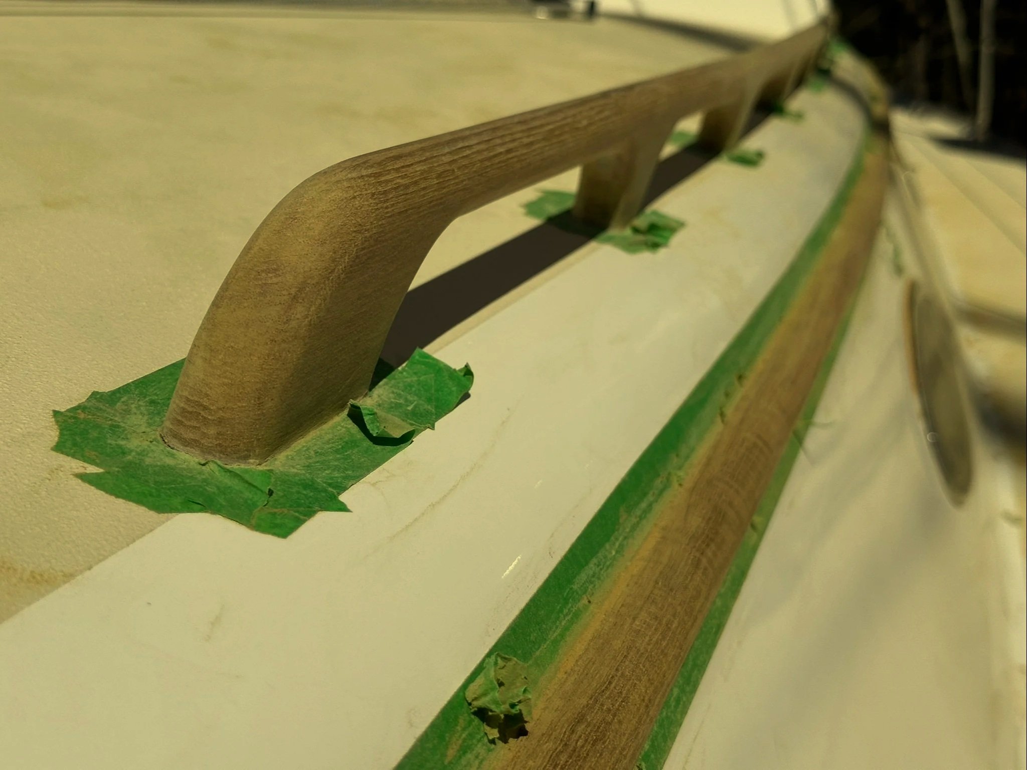 Close-up of a wooden chair armrest covered with green painter's tape on a beige surface.