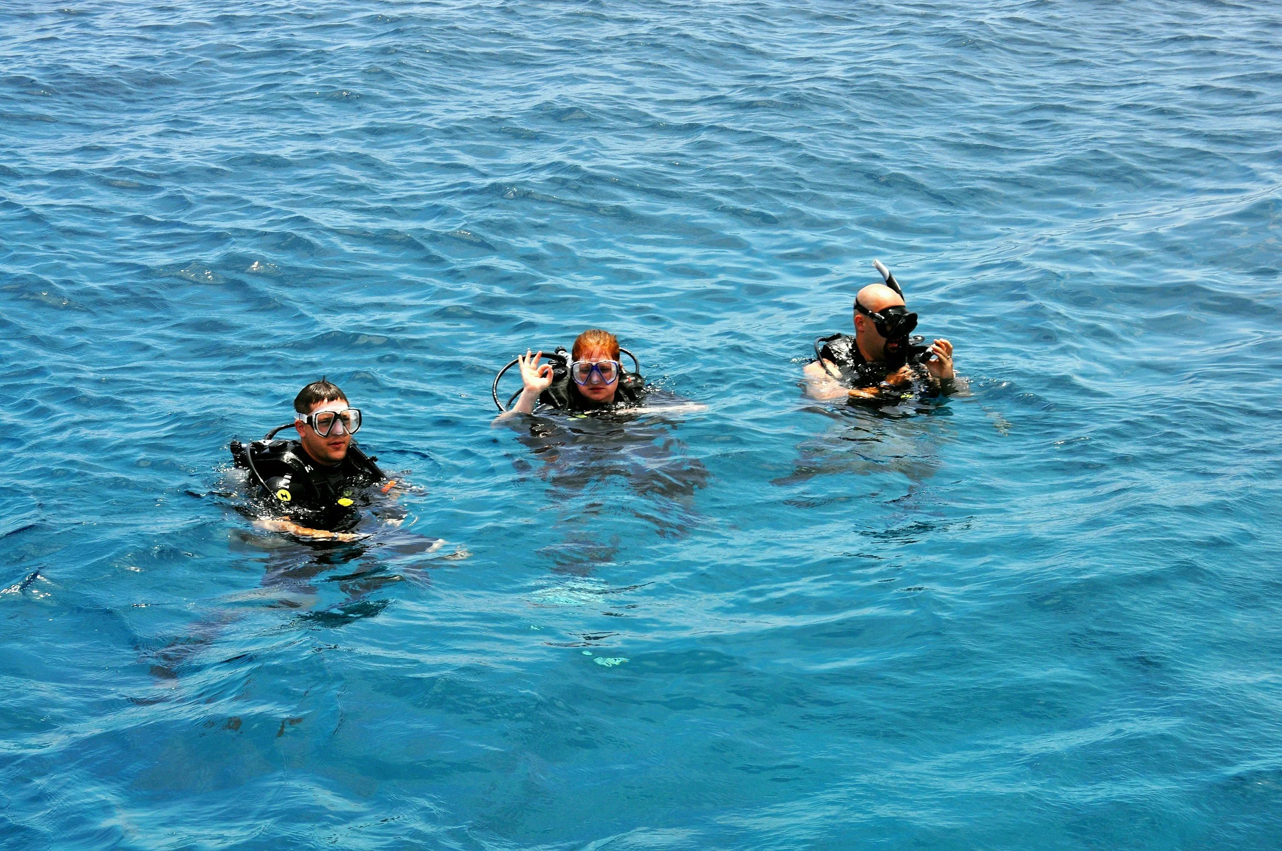 Three people in scuba diving gear floating in the water, wearing masks and snorkels.