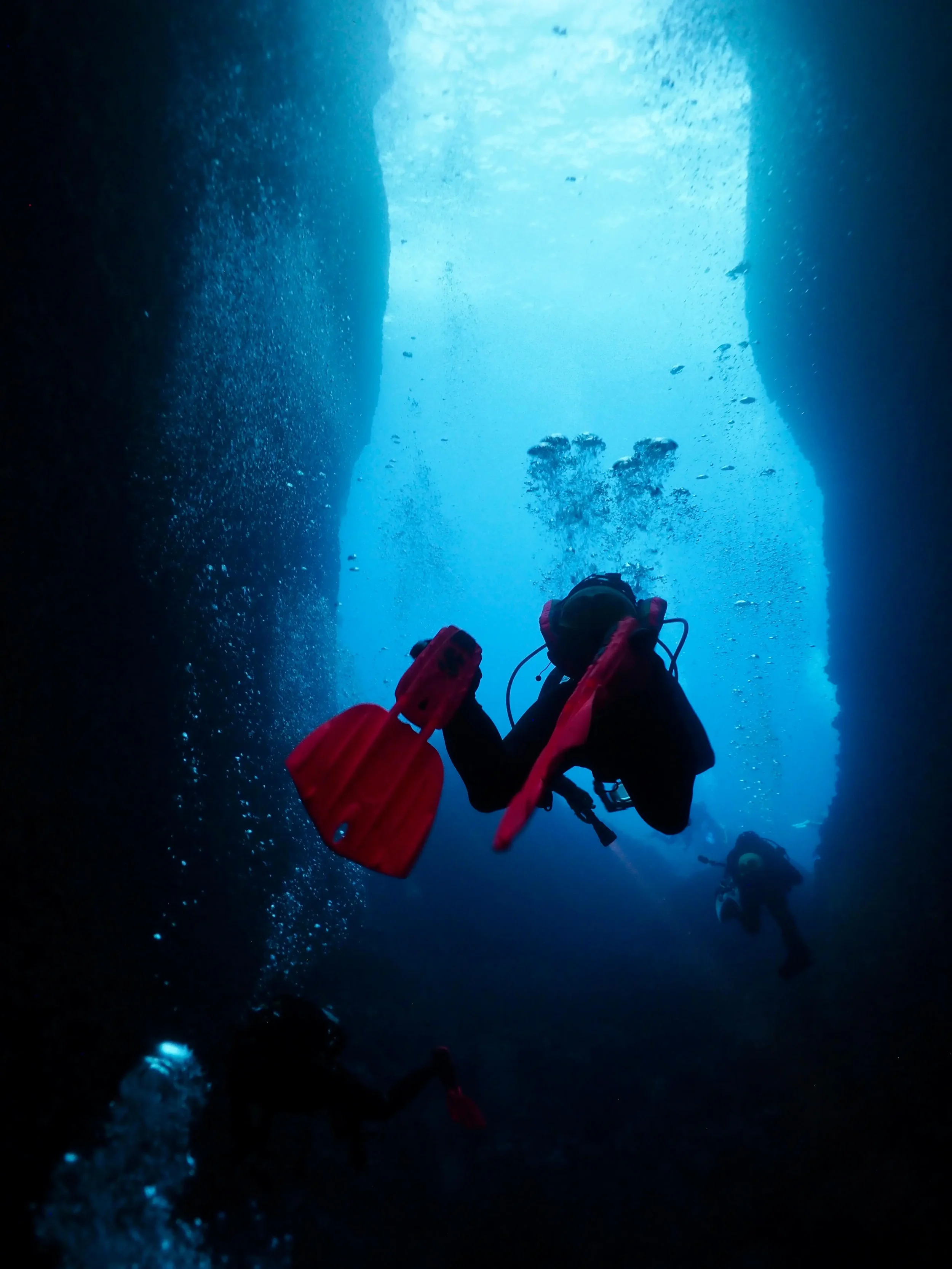 Divers exploring an underwater cave with sunlight shining from above.