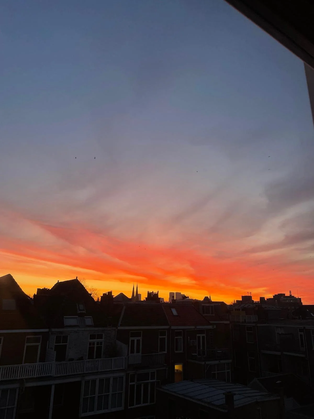 Sunset over city skyline with silhouetted buildings and colorful orange, pink, and purple clouds in the sky.