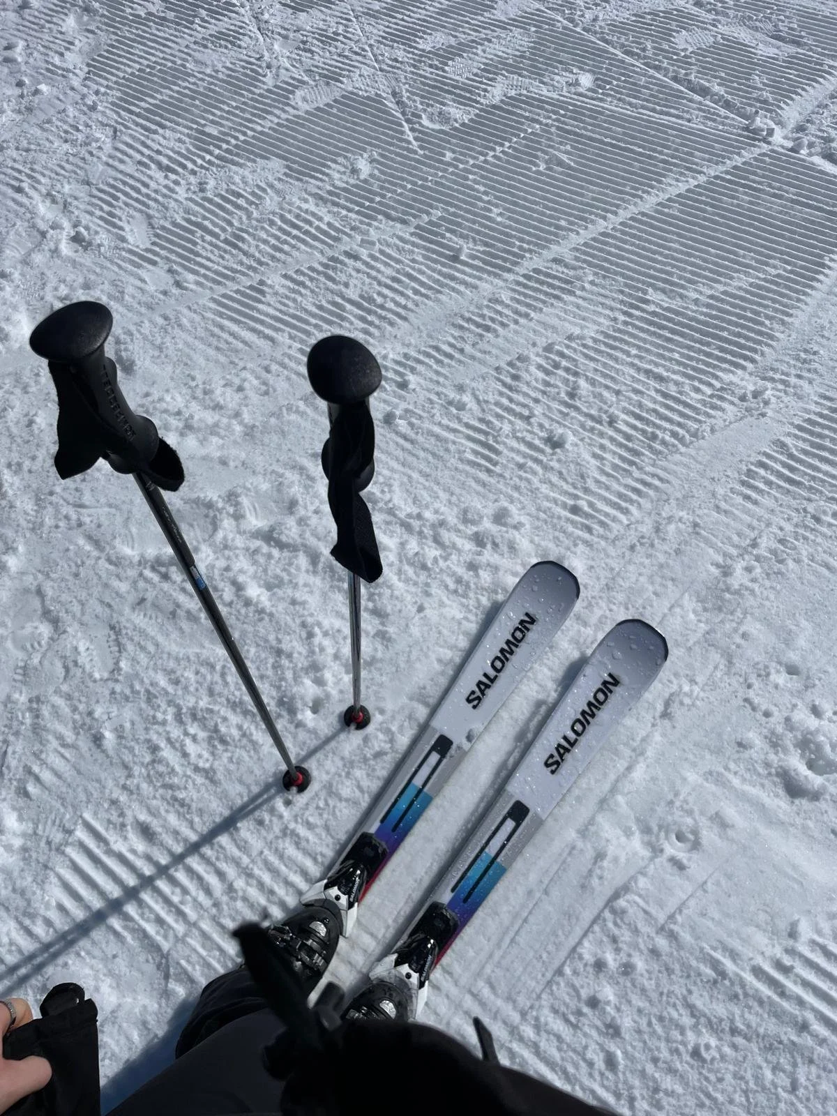 Ski poles and skis on a snowy slope with groomed snow patterns.