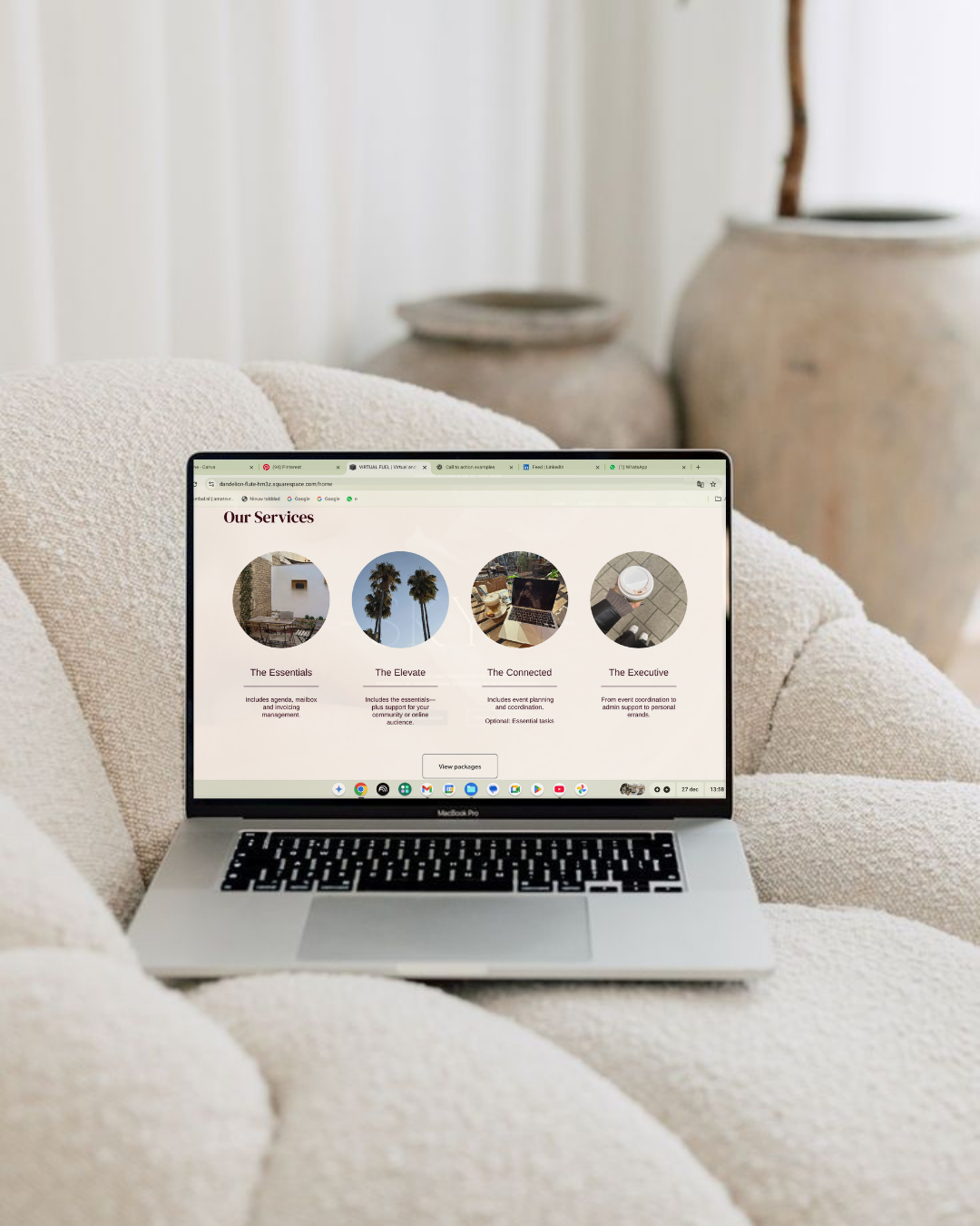 Laptop on a cream-colored couch displaying a website with service packages labeled 'The Essentials,' 'The Elevate,' 'The Connected,' and 'The Executive'.