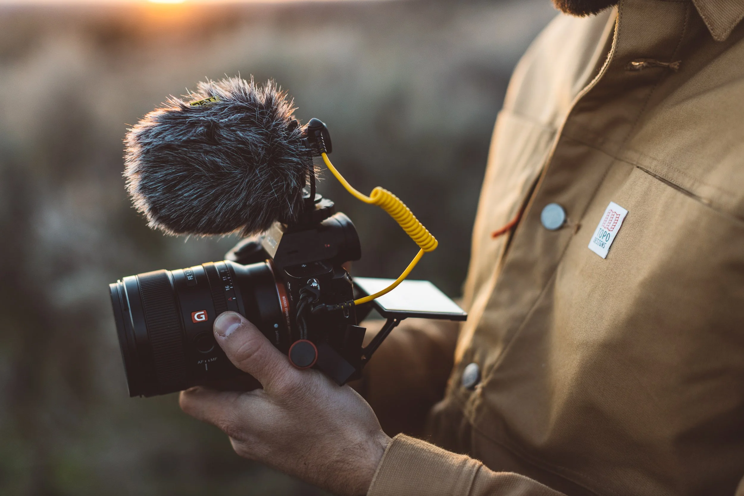 Content creator holding a sony mirrorless camera with a microphone on it in the Boise foothills during a branding photoshoot at sunset.