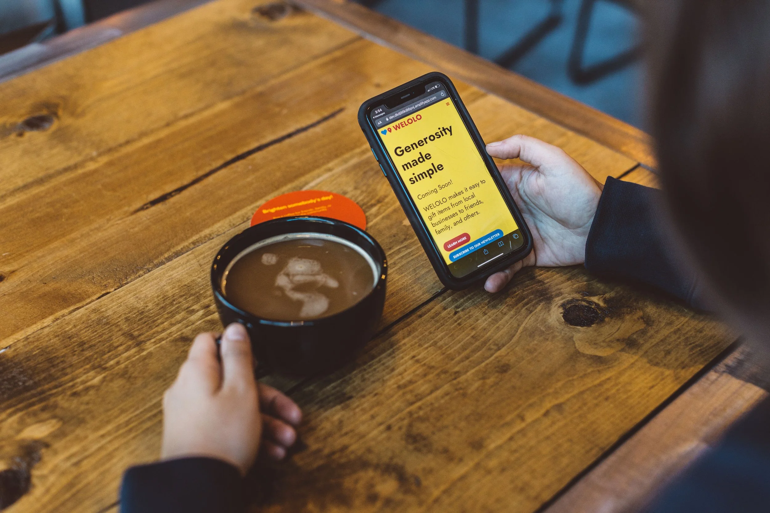 A person holding a smartphone with a website open, sitting at a wooden table with a black mug of coffee and a red coaster during a branding photoshoot in Boise, Idaho.
