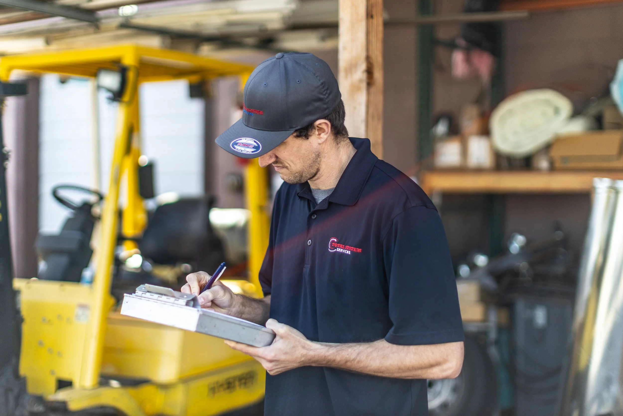 HVAC technician writing on a clipboard with a forklift in the background during a commercial photoshoot in Boise.