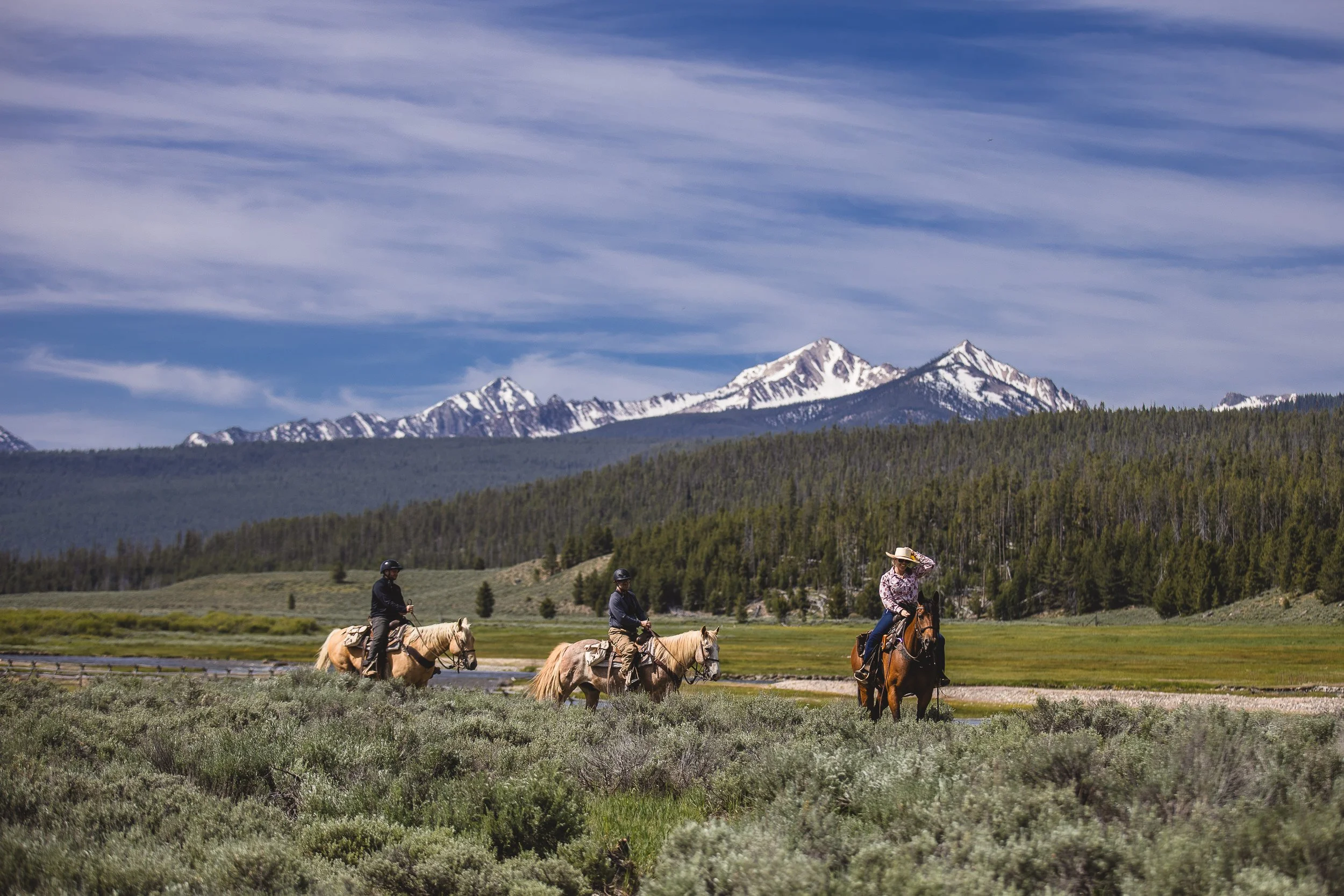 A small group of people horseback riding at Idaho Rocky Mountain Ranch, during a branding photoshoot in Stanley Idaho.