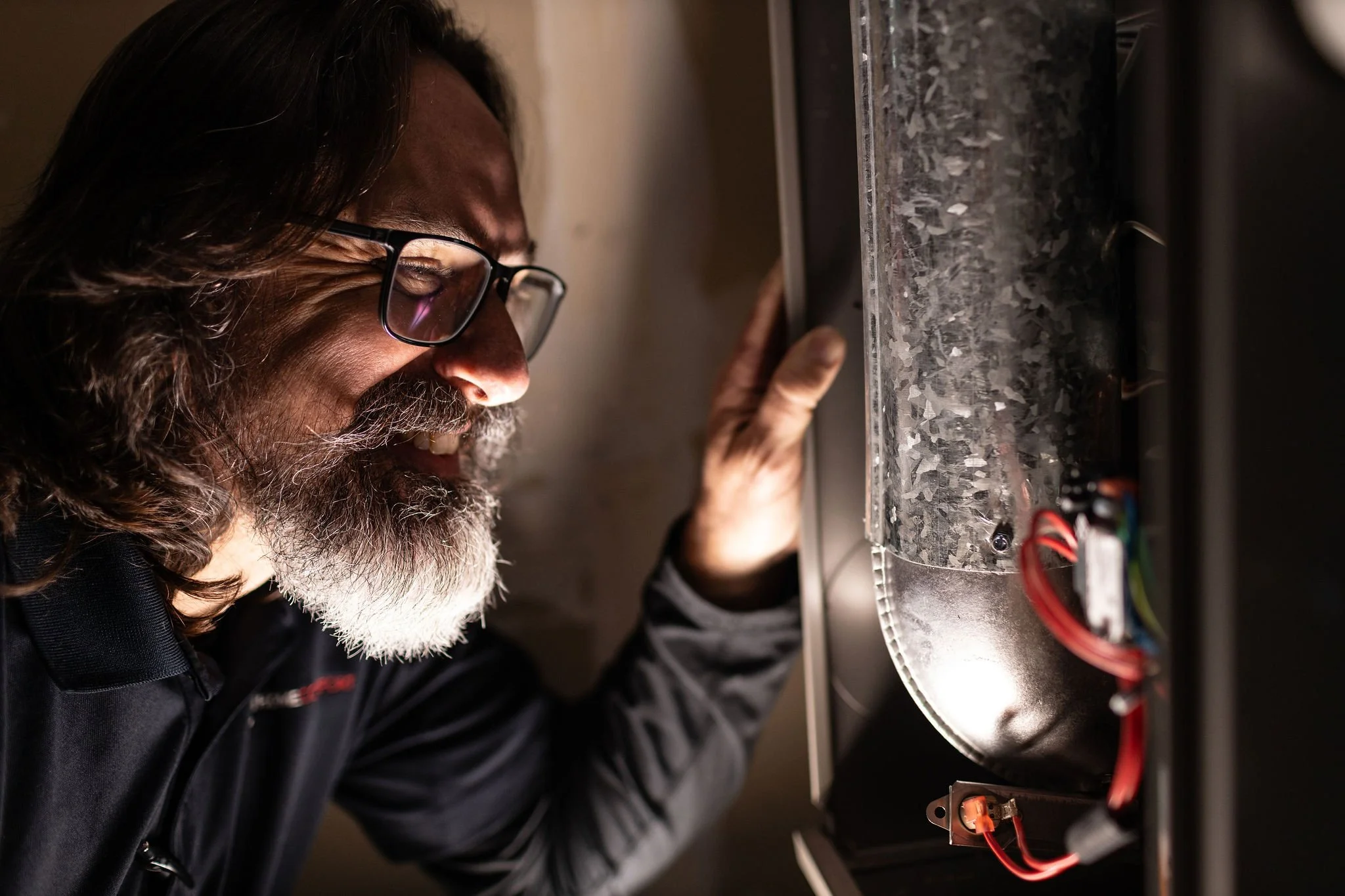 A man with glasses and a gray beard looks closely at electronic components inside a metallic enclosure.