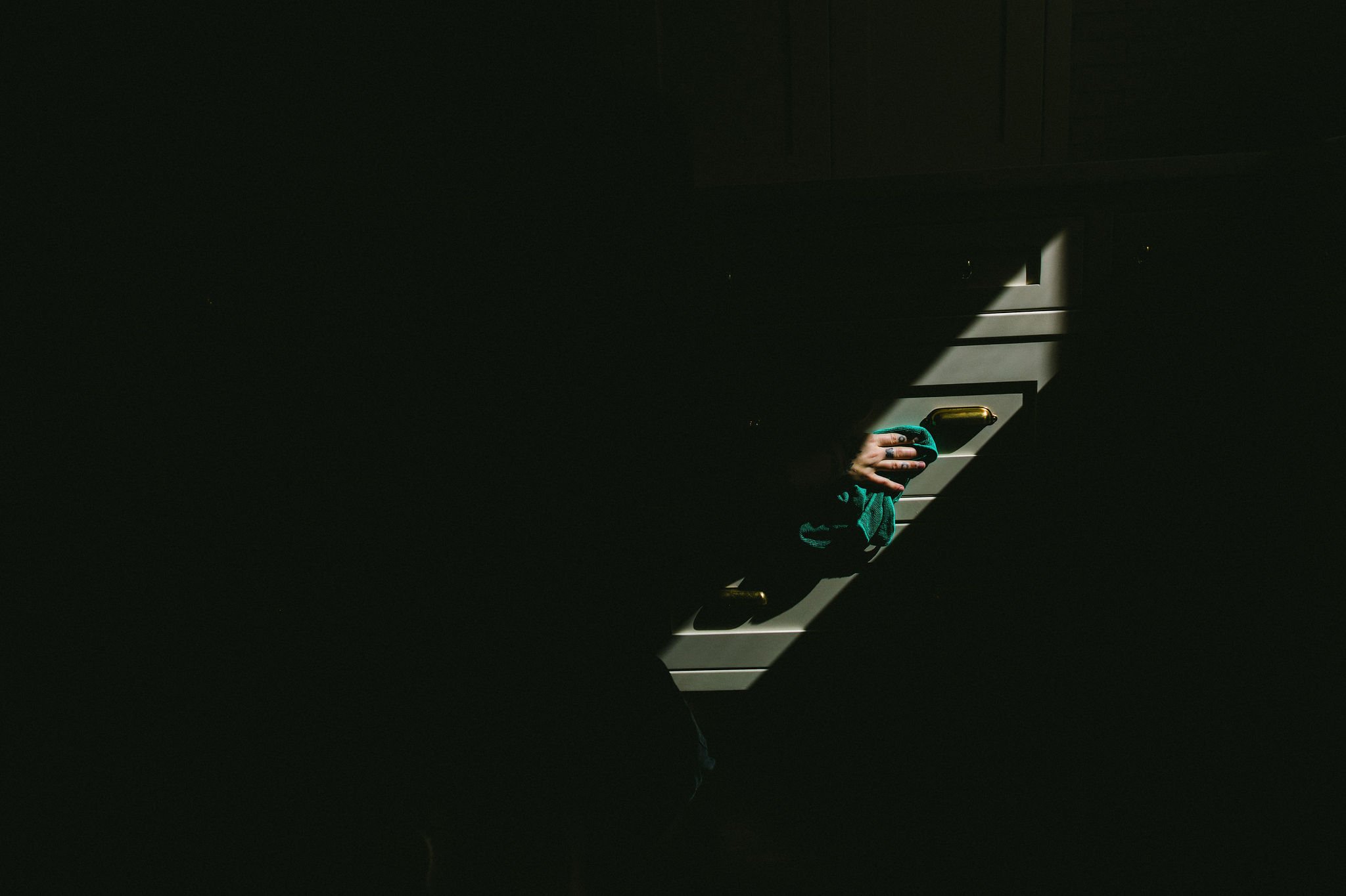 A hand holding a cleaning cloth on a kitchen stove in Boise, Idaho during a branding photoshoot, with sunlight casting shadows across the scene.