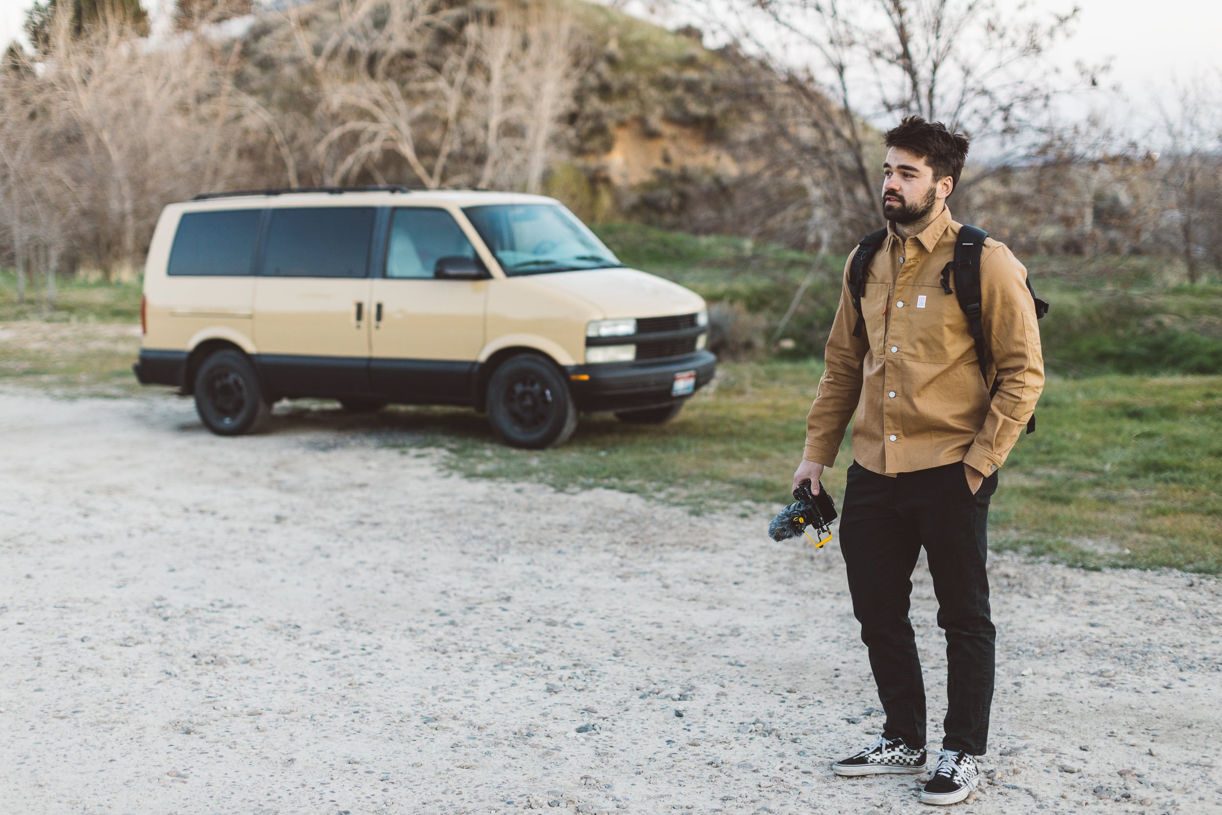 Boise content creator standing in the Boise foothills, holding his camera with his van in the background.