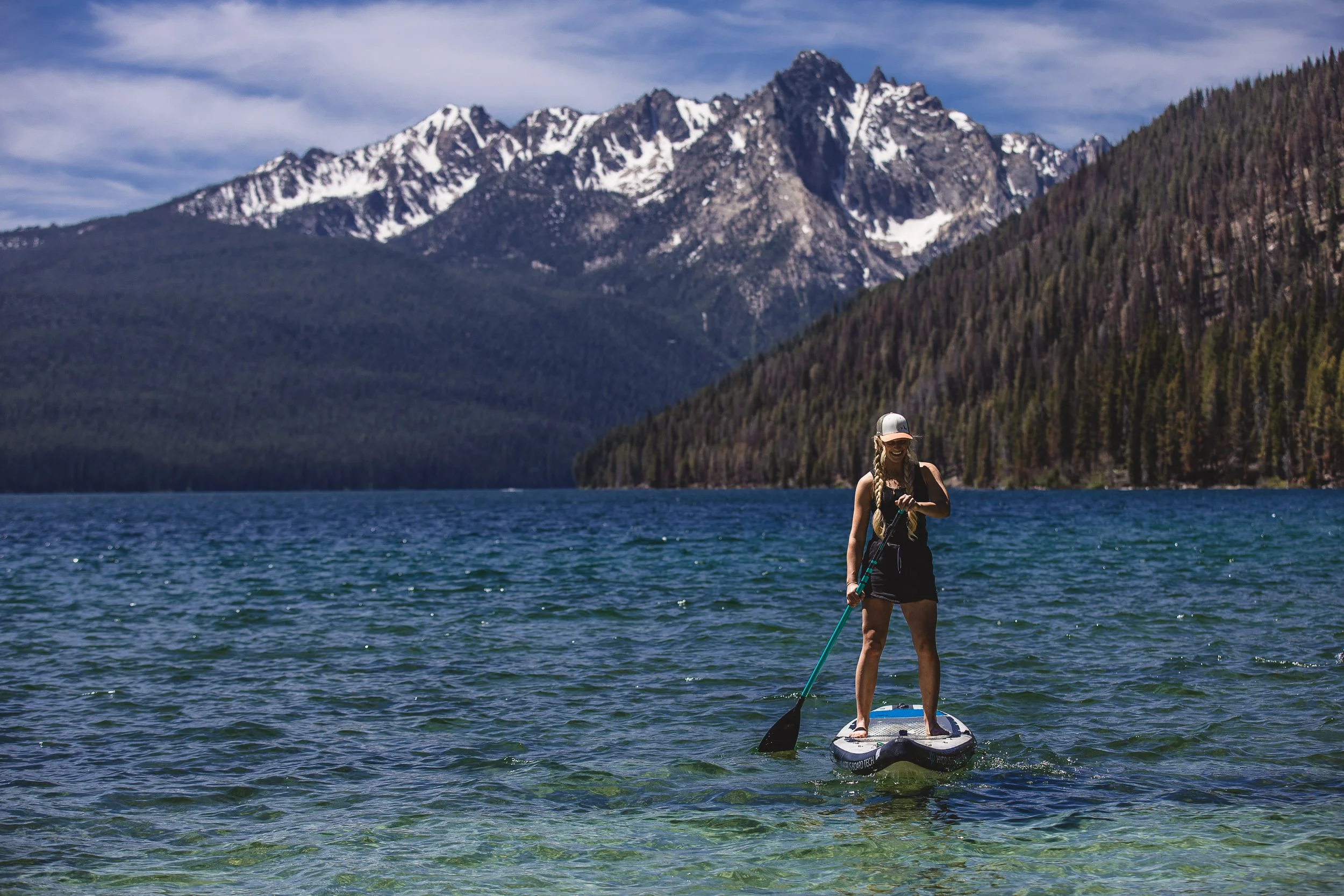 Woman smiling while paddle boarding in Redfish Lake at the base of the Sawtooth Mountains, during a branding photoshoot in Stanley Idaho.