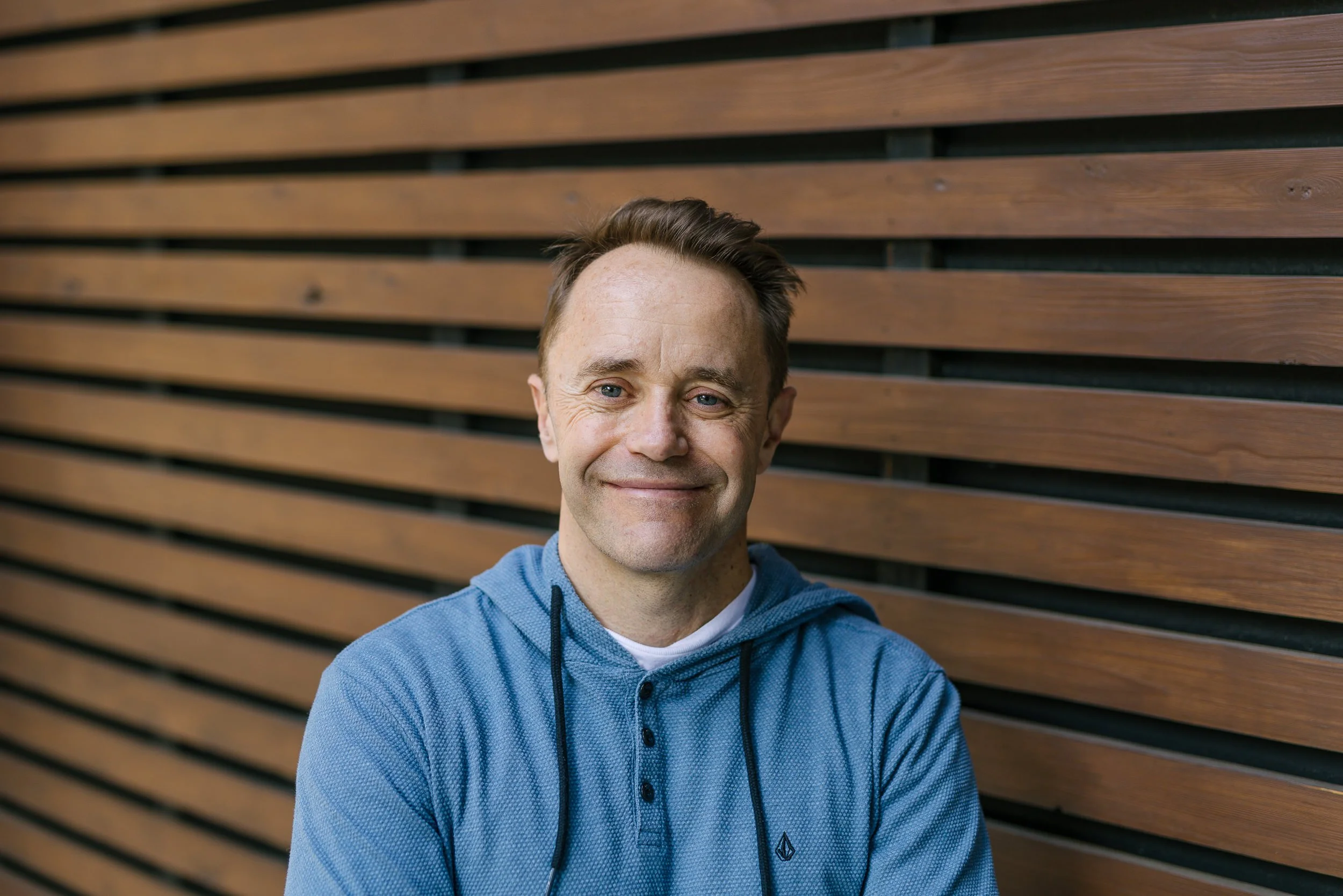 Business owner smiling in front of wooden wall in downtown Boise during a branding photoshoot.