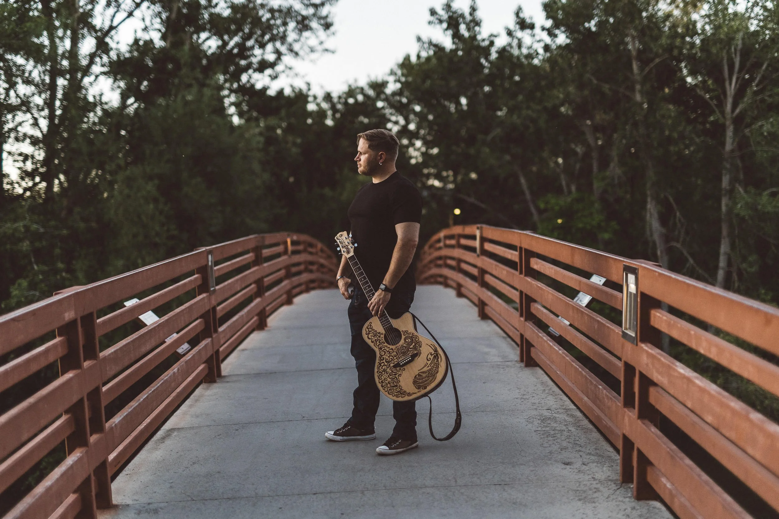 Man holding a guitar looking off into the distance during a branding photoshoot on Friendship Bridge in Julia Davis Park in Boise.