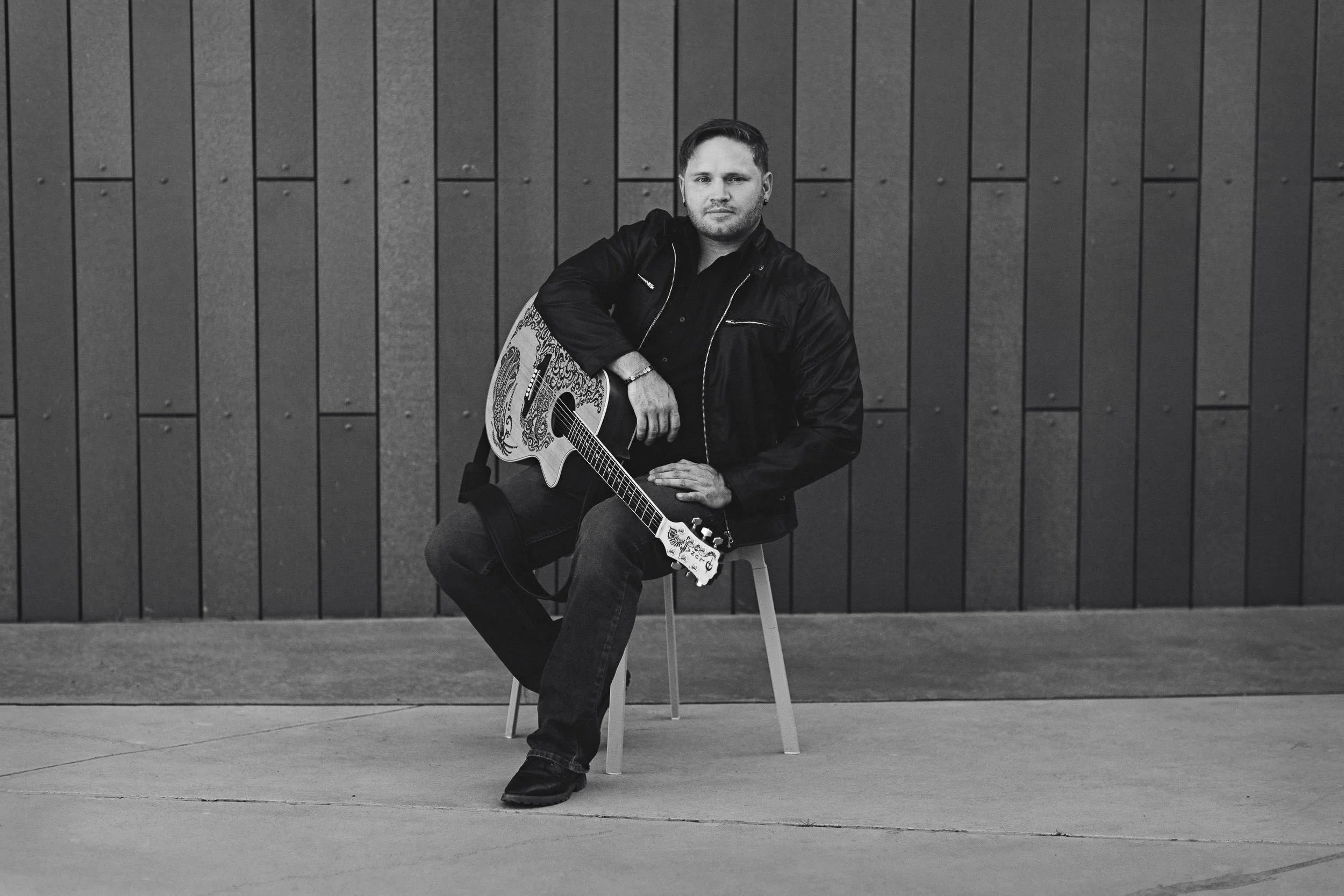 Guitarist sitting in front of a wall looking at camera while holding a guitar during a personal branding photoshoot in Boise.