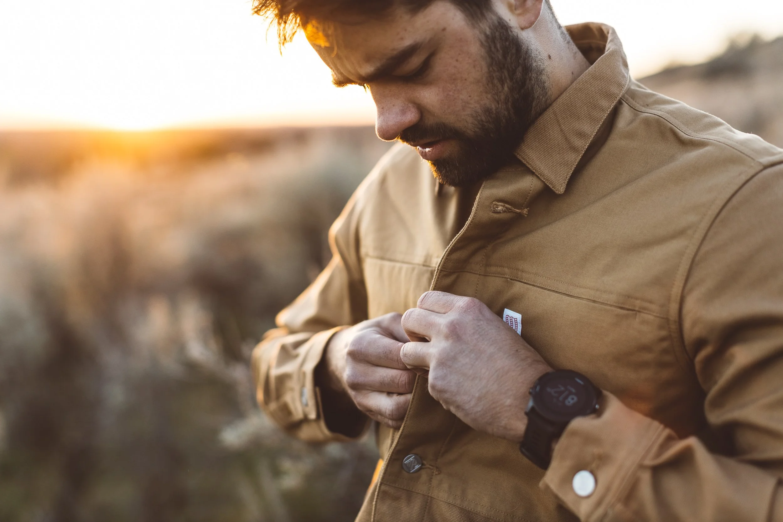 Young creative entrepreneur buttons up jacket in the Boise foothills during a branding photography session at sunset.