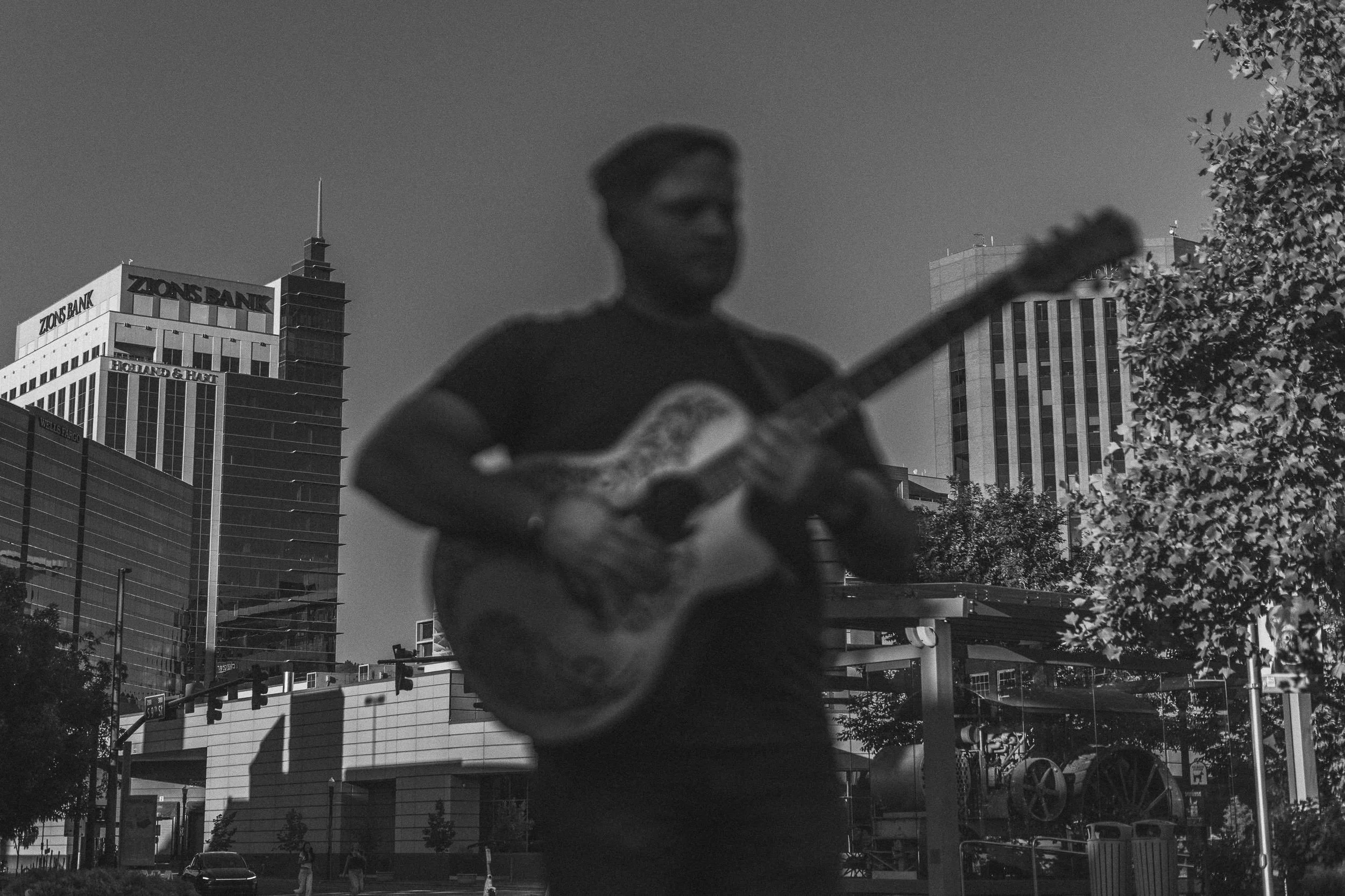 Man playing a guitar with the buildings of downtown Boise in the background during a branding photoshoot.