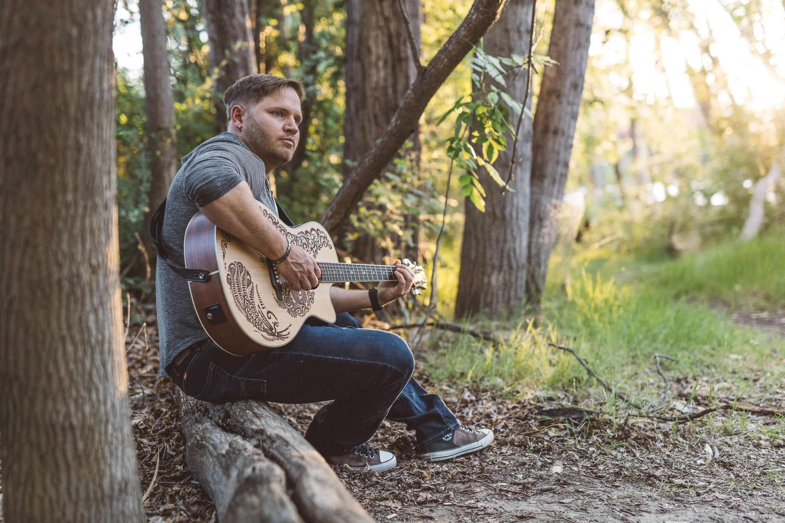 Musician sitting on log playing guitar at sunset during a branding photoshoot on the Boise River Greenbelt in downtown Boise.