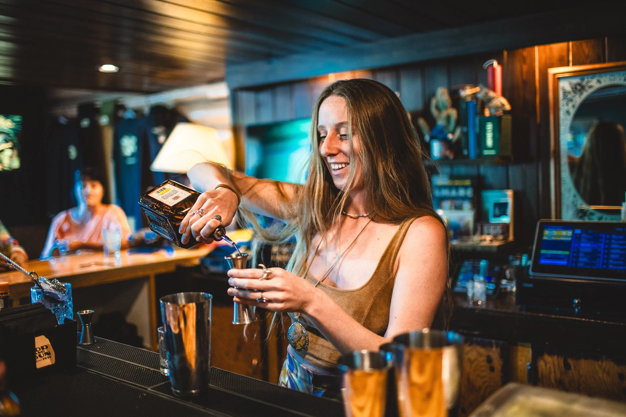 Bar tender pouring a drink and smiling at Rod and Gun, during a branding photoshoot in Stanley Idaho.