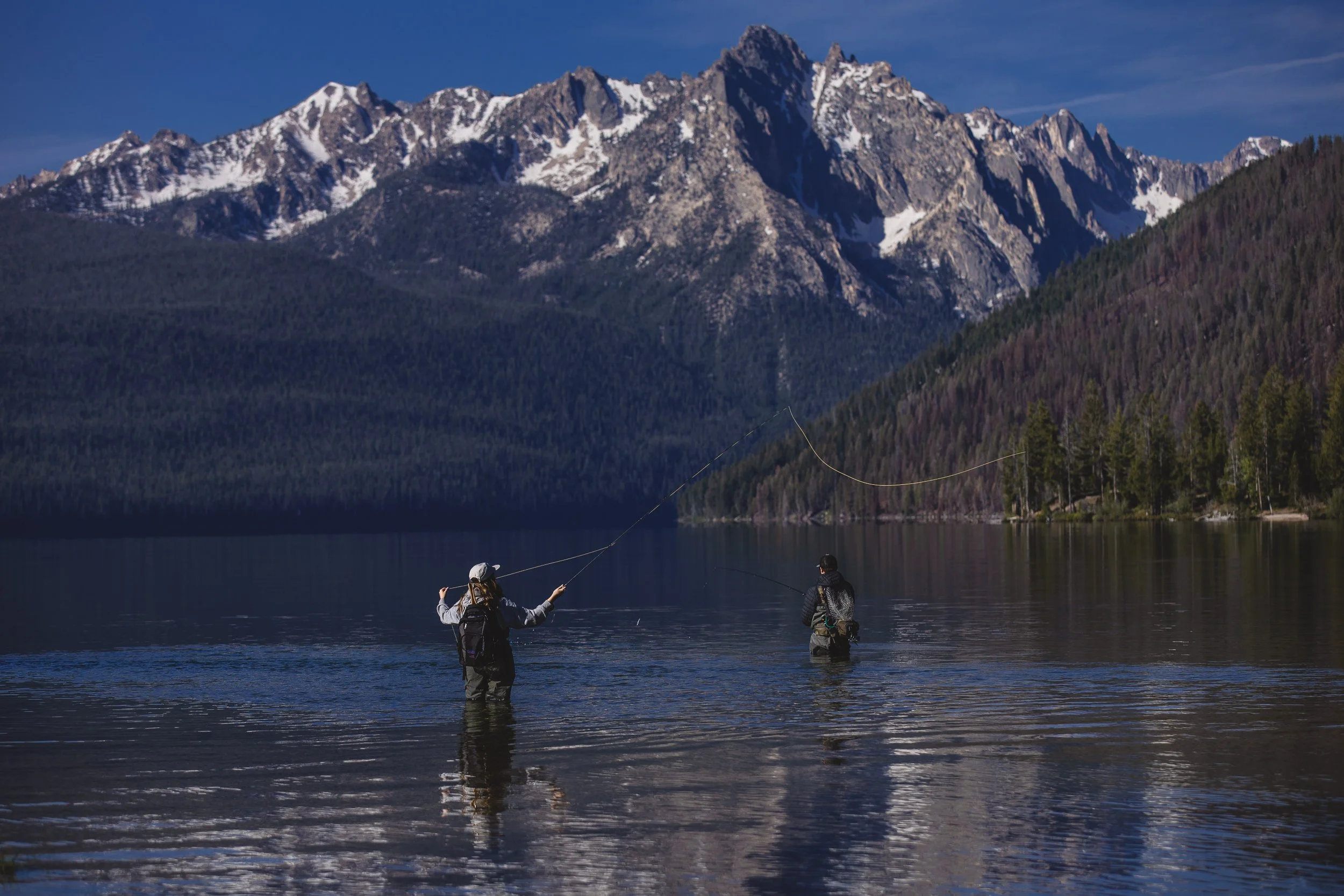 Couple fly fishing in Red Fish Lake at the base of the Sawtooth Mountains, during a branding photoshoot in Stanley, Idaho.