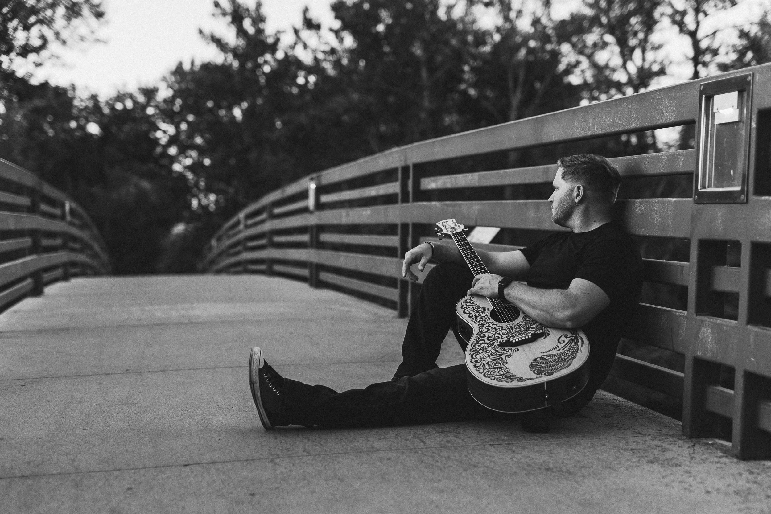 Guitarist holding guitar and looking away from the camera sitting on friendship bridge in Julia Davis Park during a branding photoshoot in Boise.