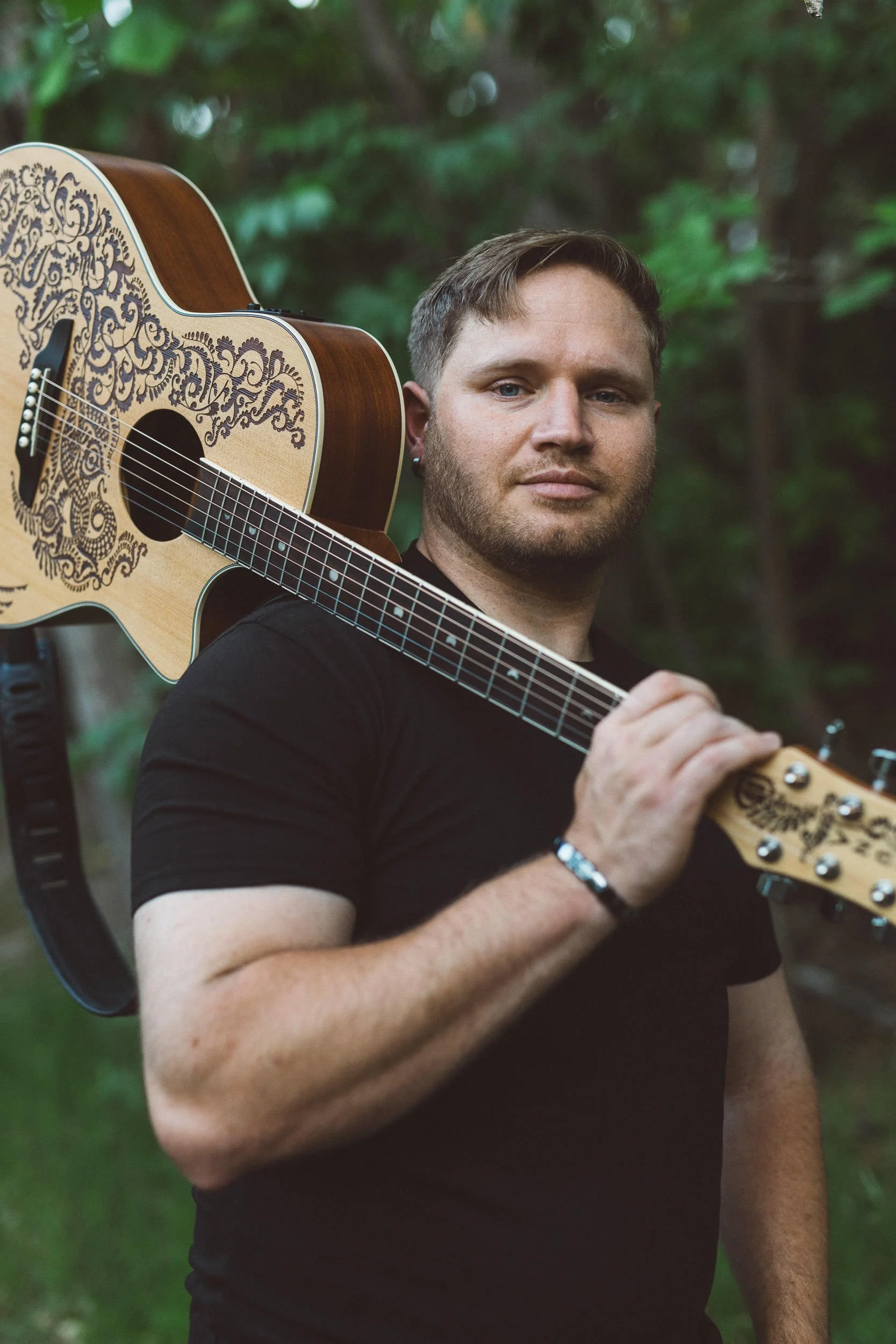 Man with blue eyes holding guitar over his shoulder during a branding photoshoot on the Boise River Greenbelt.