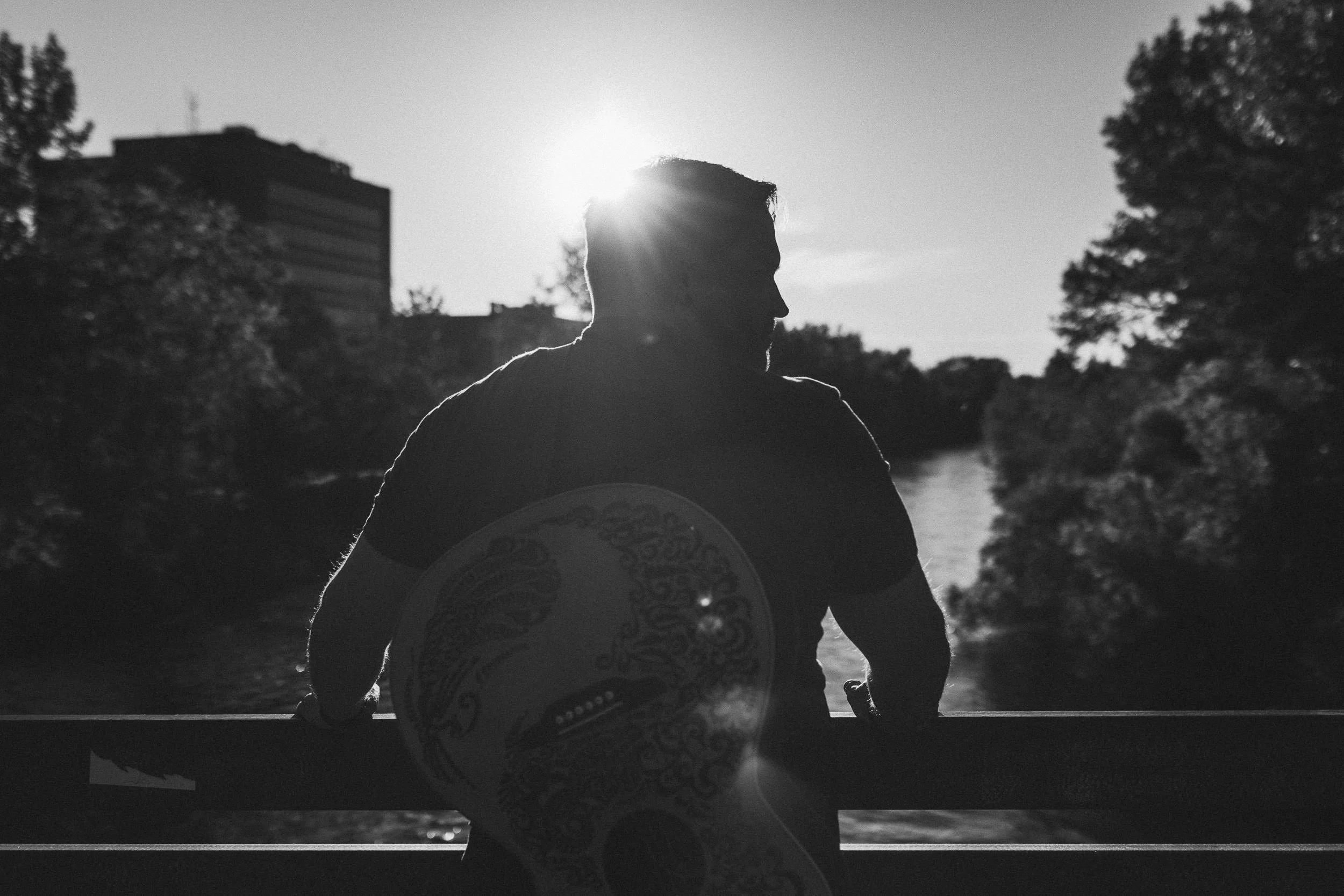 Musician with guitar on his back looking away from the camera during a branding photoshoot on the Boise River Greenbelt.