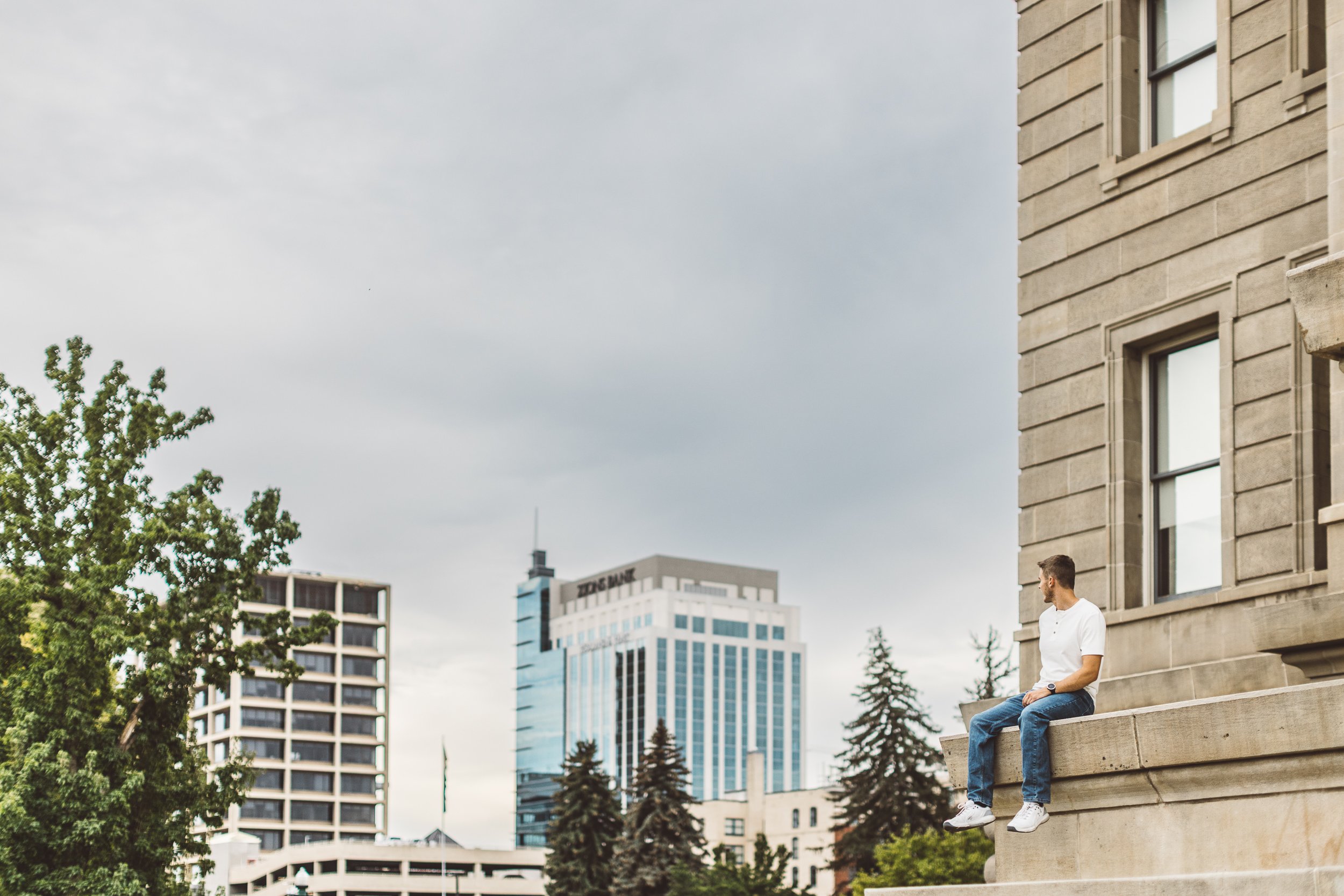 Entrepreneur sitting confidently on a ledge at the Idaho State Capitol with downtown Boise in the background during a professional personal branding photoshoot for business owners in Boise Idaho.