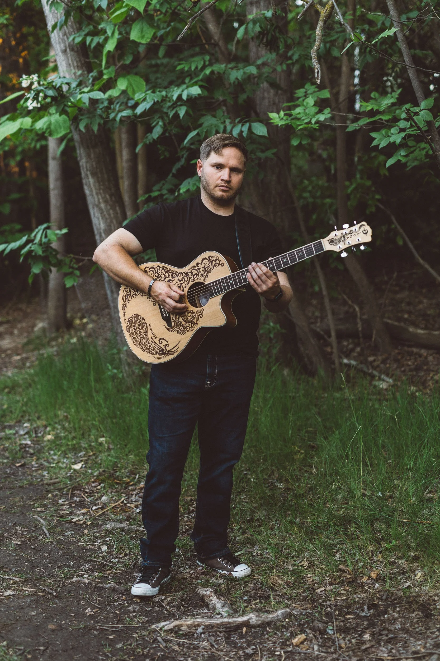 Man playing guitar while looking at the camera during a branding photoshoot on the Boise River Greenbelt.