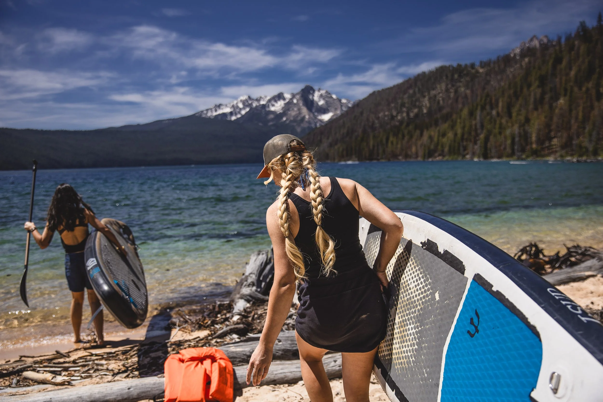 Two women carrying paddle boards at Redfish Lake during a branding photoshoot in Stanley Idaho.