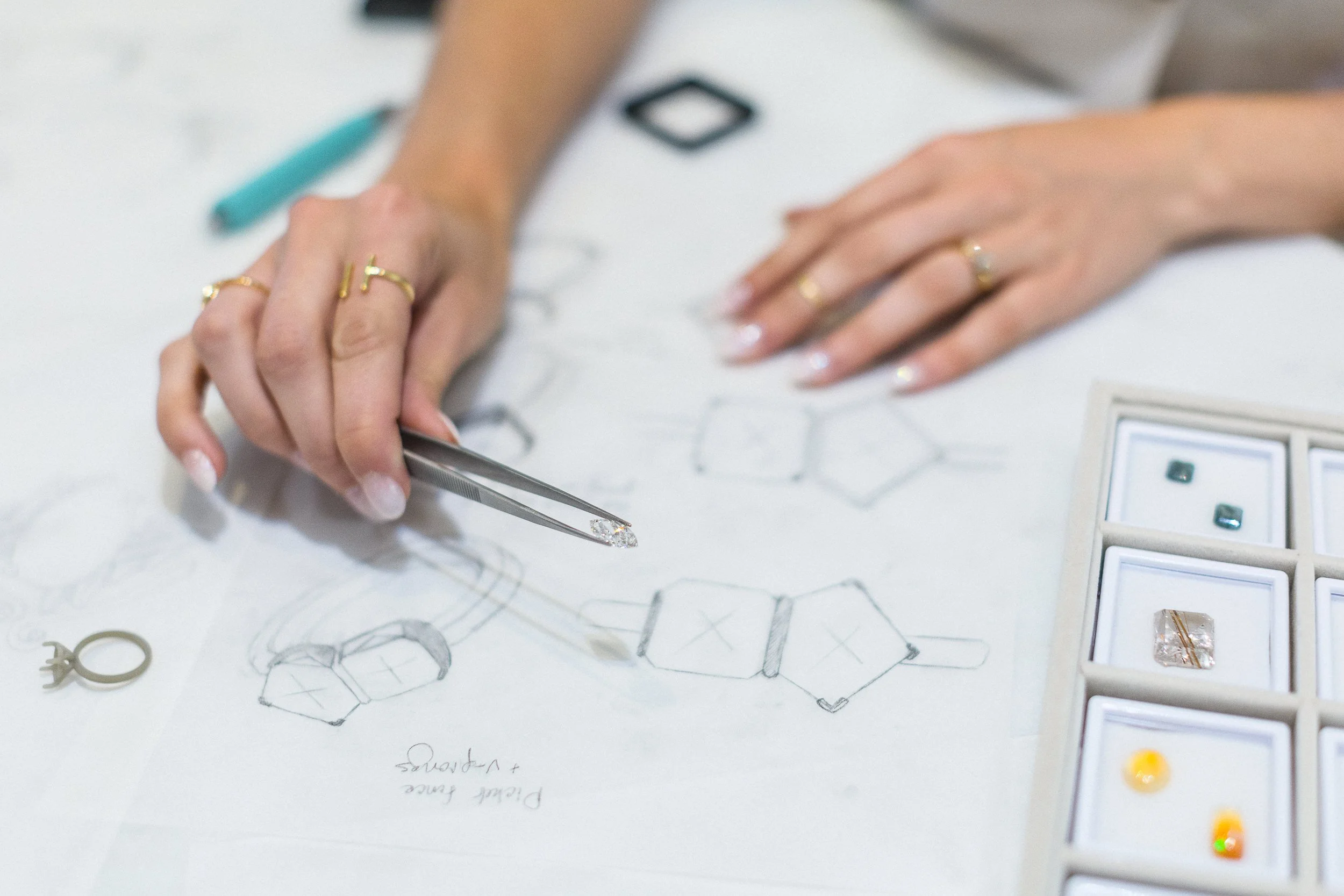 Lifestyle photo of a custom jewelry maker holding a diamond above custom jewelry drawings in a jewelry shop during a branding photoshoot in downtown Boise.