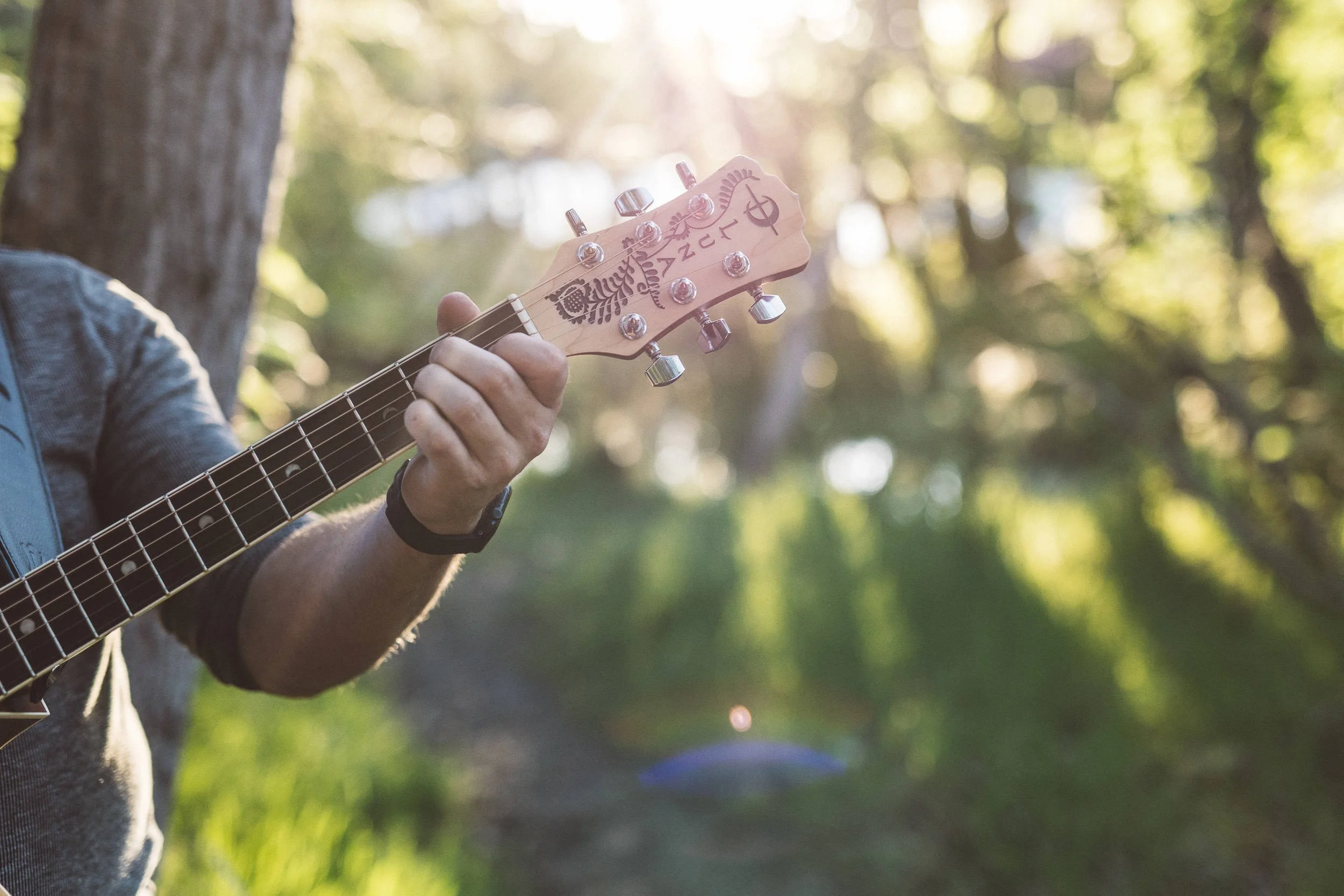 Neck of a Luna brand guitar backlit by the sun during a branding photoshoot on the Boise River Greenbelt.